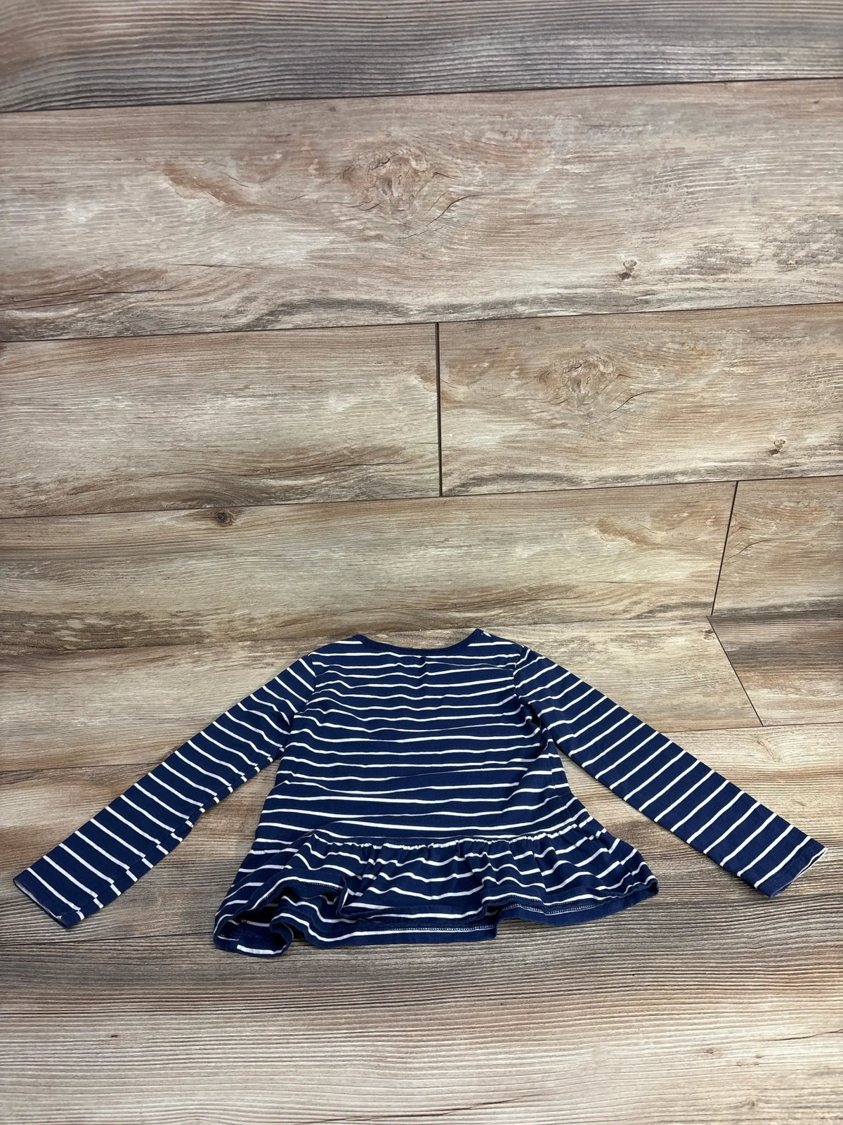 Front view of Carter's navy and white striped long-sleeve peplum top with ruffled hem on wood plank floor