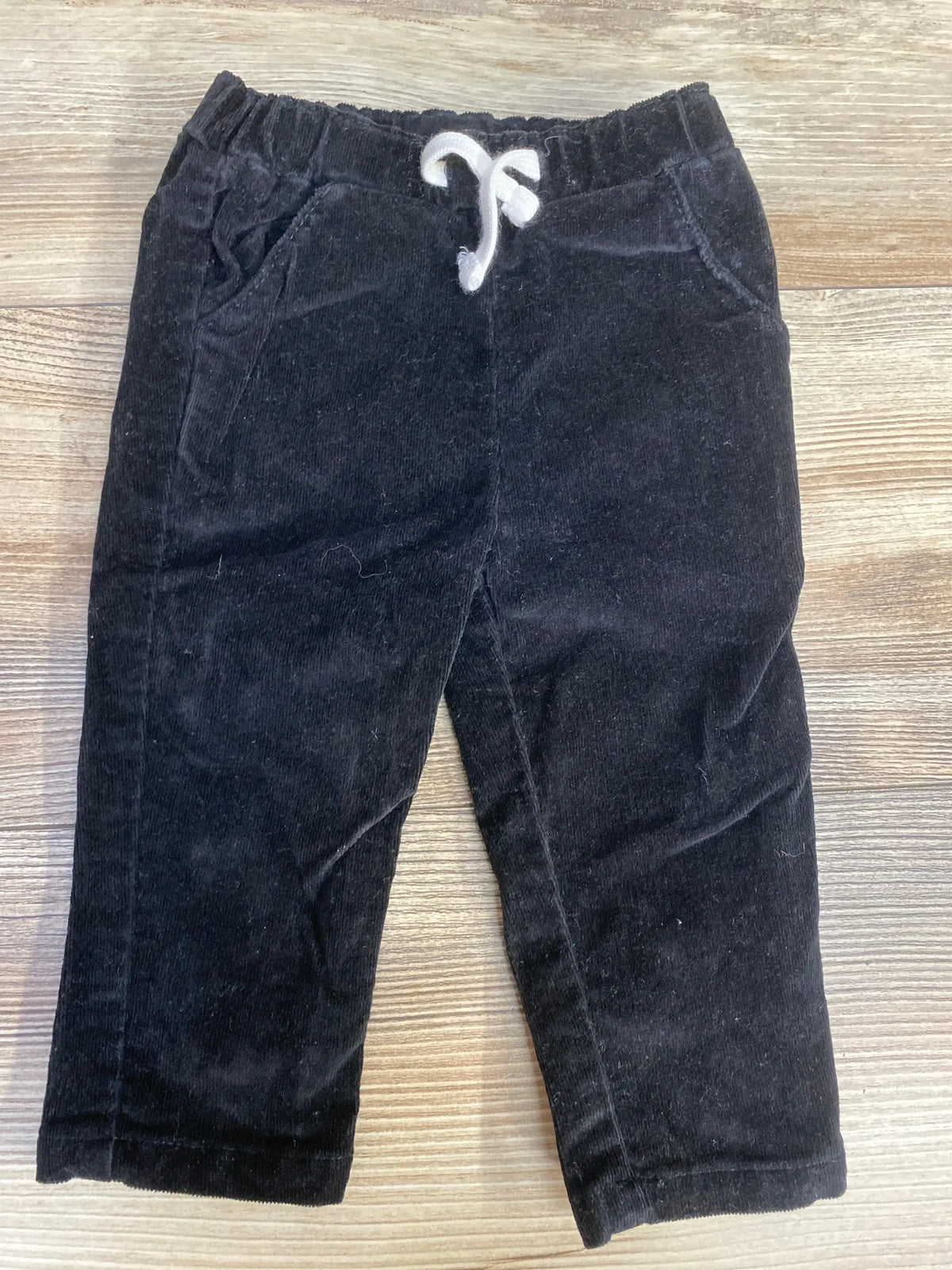 Black toddler corduroy pants with white drawstring laid flat on wood background
