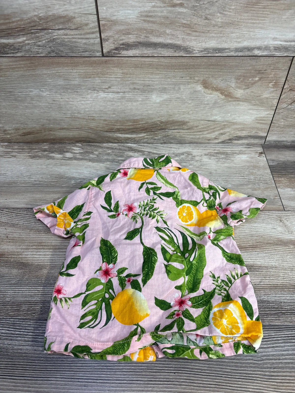Back view of pink toddler linen-blend button-up shirt showcasing lemon and green leaf print on wood floor