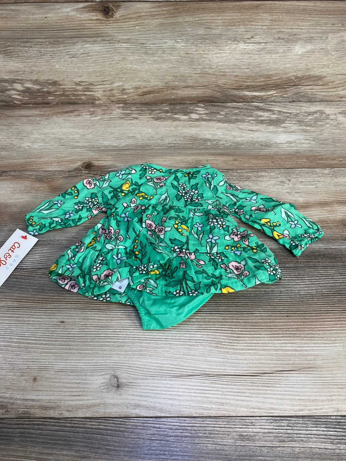 Flat lay of newborn green floral Henley dress with matching bloomers showing long sleeves and tiered ruffle skirt on wood background