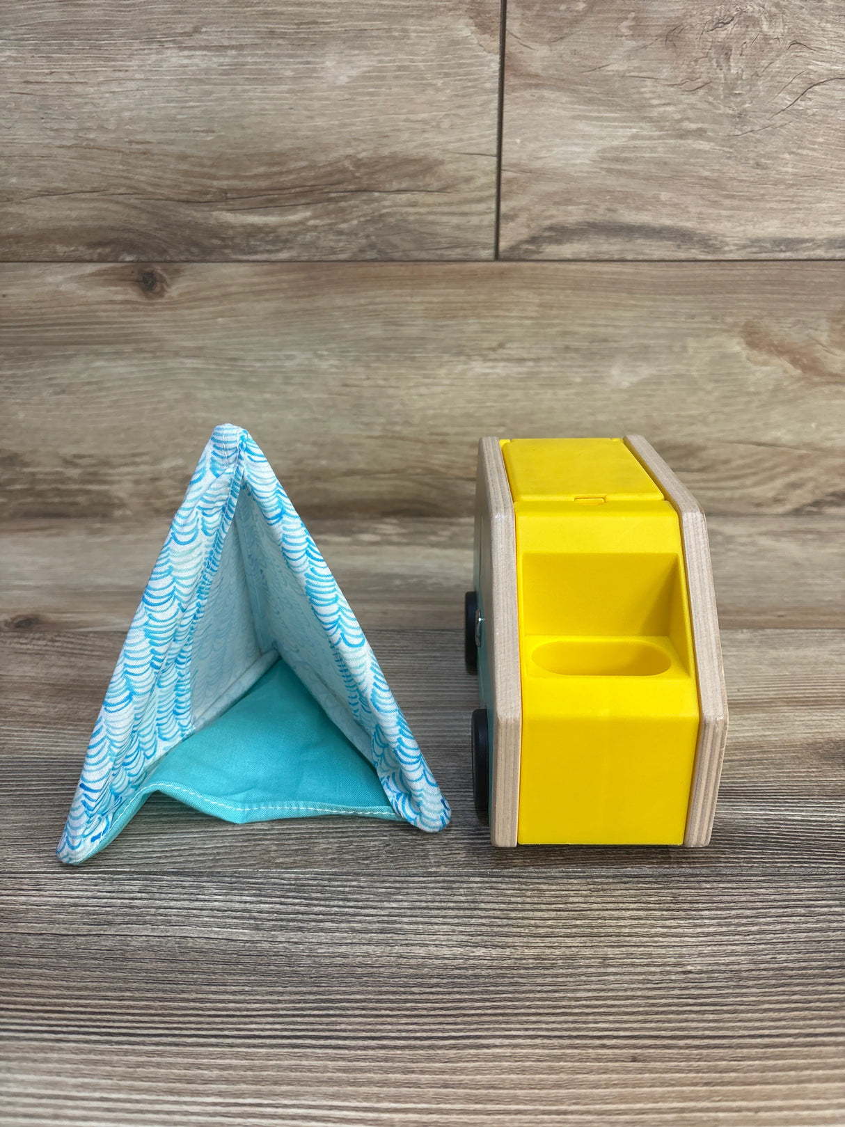 Wooden yellow toy car and blue fabric play tent on wood surface