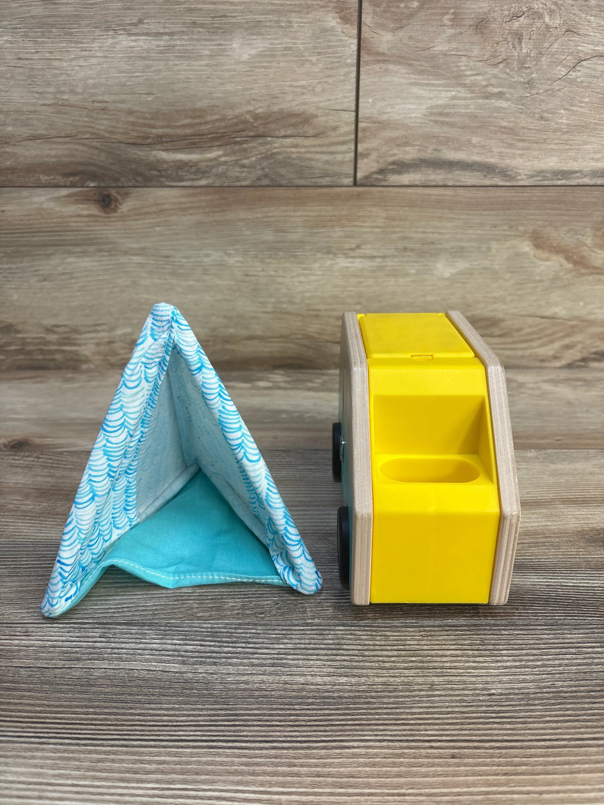 Wooden yellow toy car and blue fabric play tent on wood surface