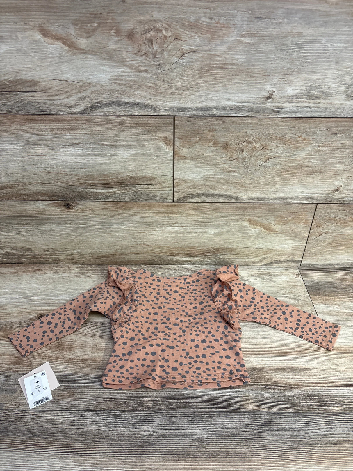 Flat lay of Grayson mini ruffled polka dot top, brown 18M, showing ruffle shoulder details and black dots on wood floor