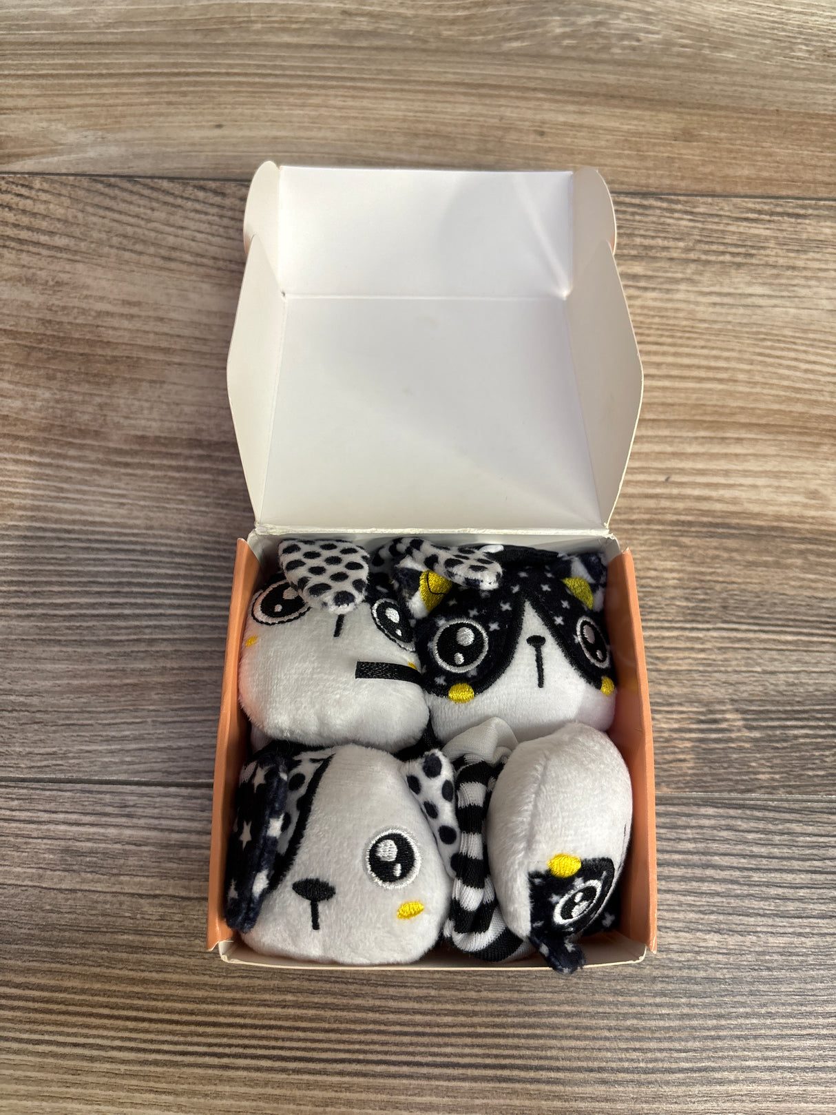 Box of black and white dog plush toys with spotted ears on wooden surface