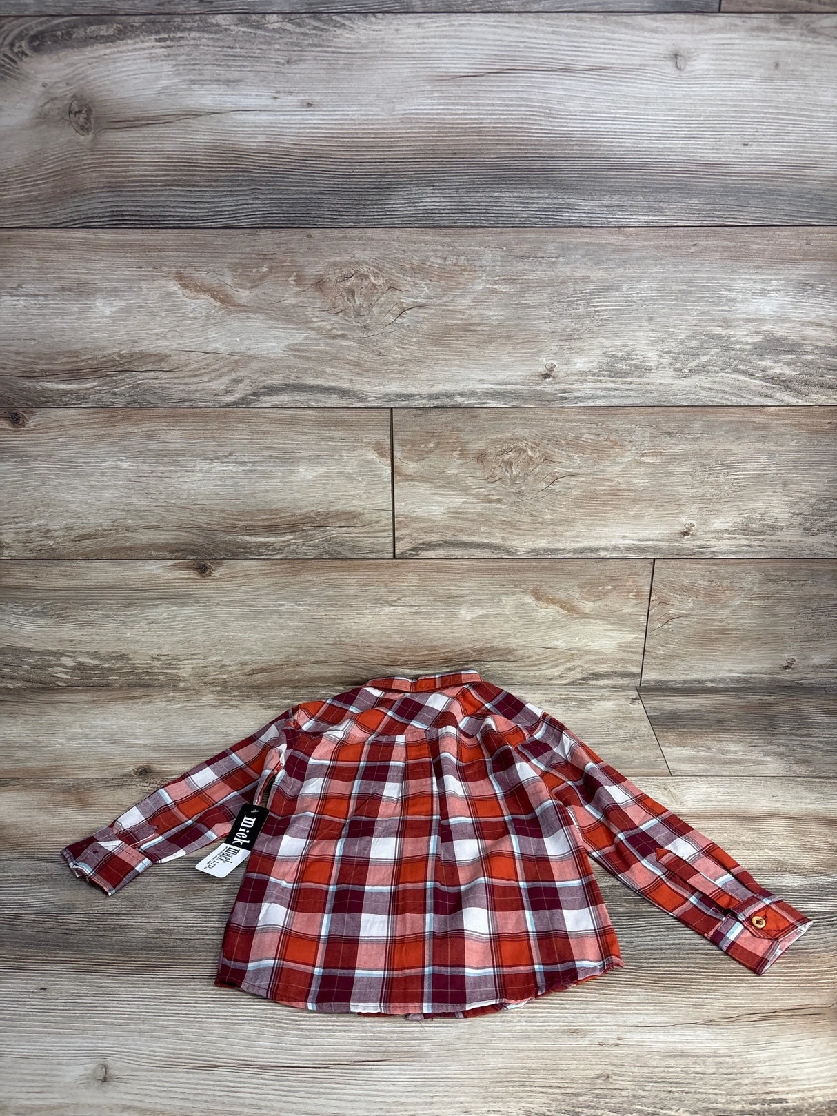 Red and white plaid long sleeve toddler shirt laid flat on wood floor