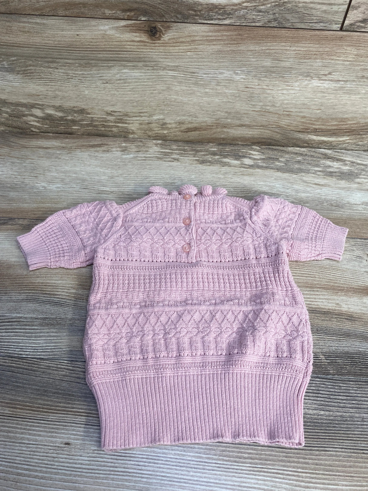 Flat lay of peach toddler sweater top (12–18M) showing diamond and cable knit, short sleeves, back buttons on wood background