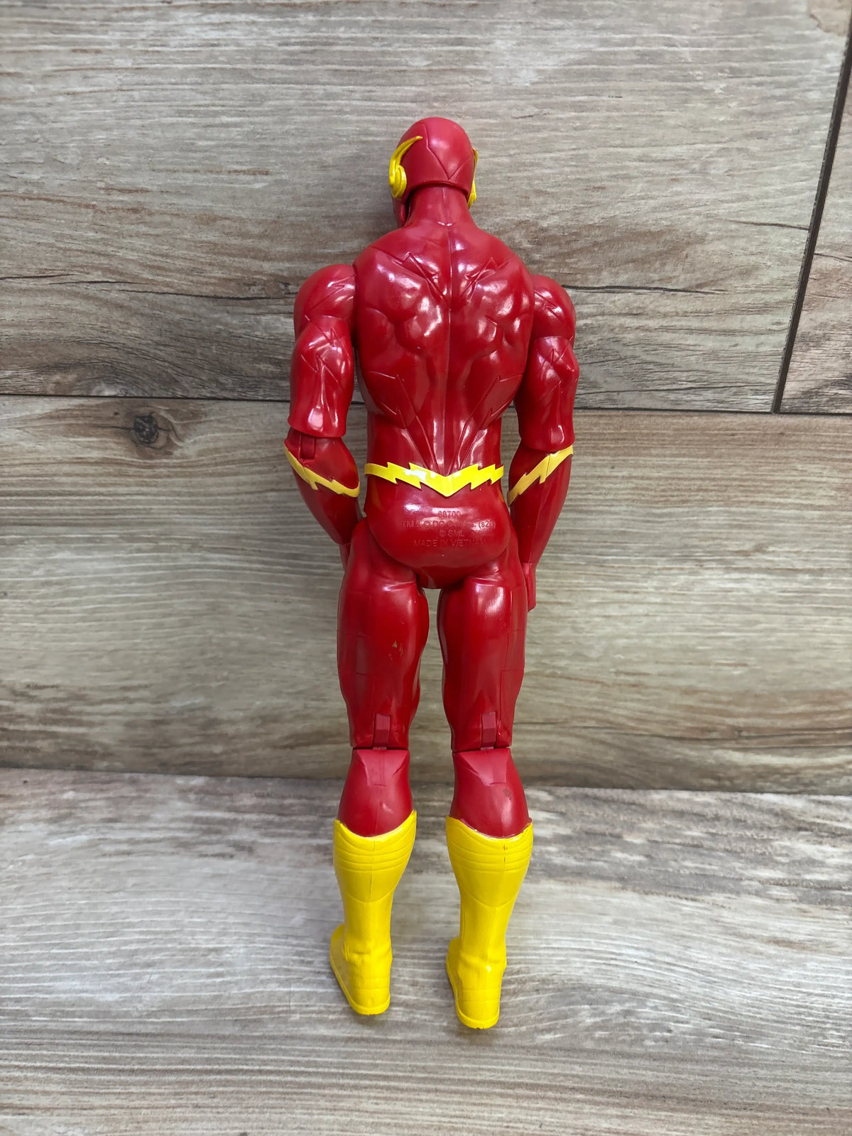 Rear view of DC Comics 12-inch The Flash action figure showcasing red and yellow costume details against a wood-grain background