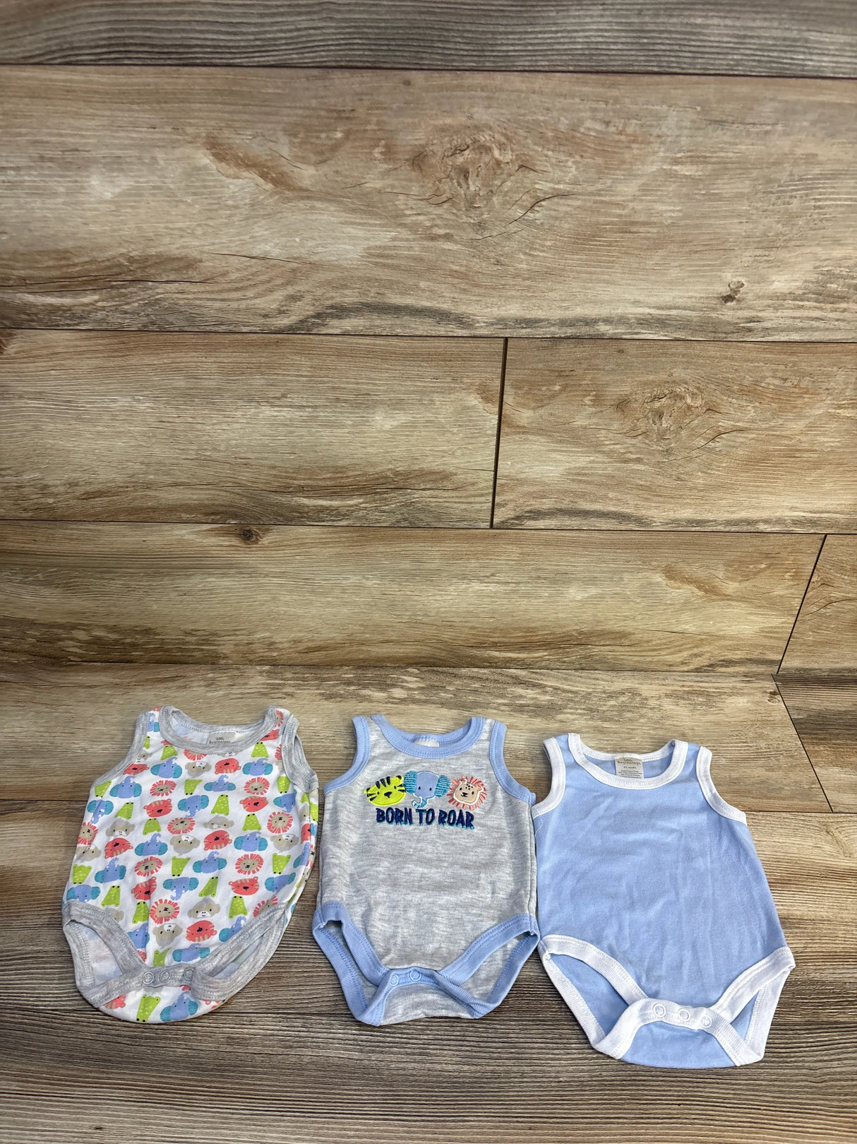 Three sleeveless baby bodysuits on wood floor, featuring animal and solid blue designs
