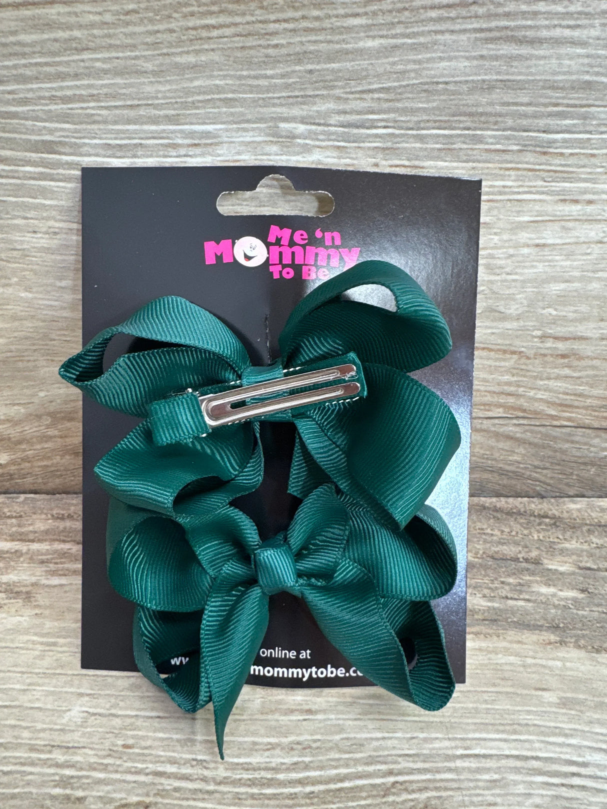 Top-down view of medium green hair bows (2-pack) showing silver alligator clips on black branded card over light wood background