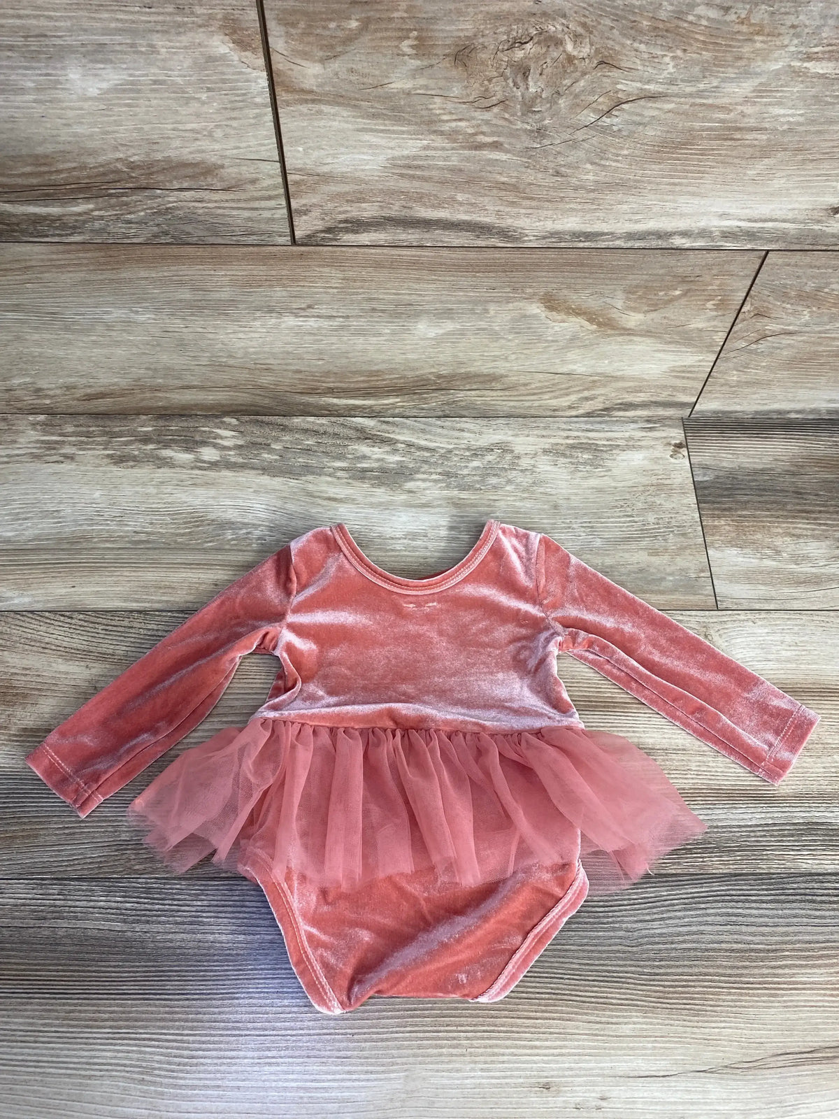 Pink velvet baby bodysuit with long sleeves and tulle tutu skirt on wooden floor