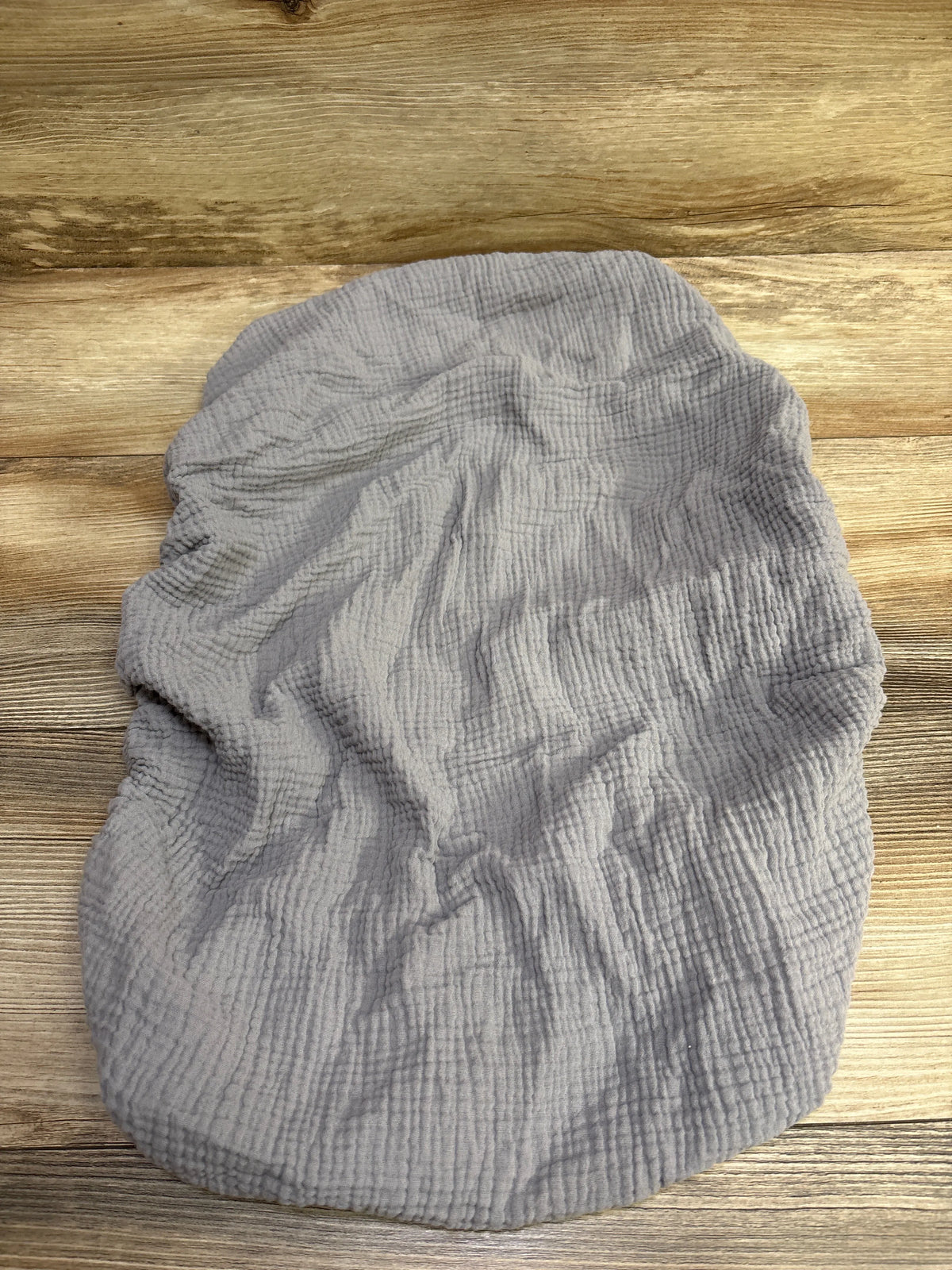 Top view of a grey muslin fitted bassinet sheet showcasing gathered elastic edges and textured fabric on a wood surface