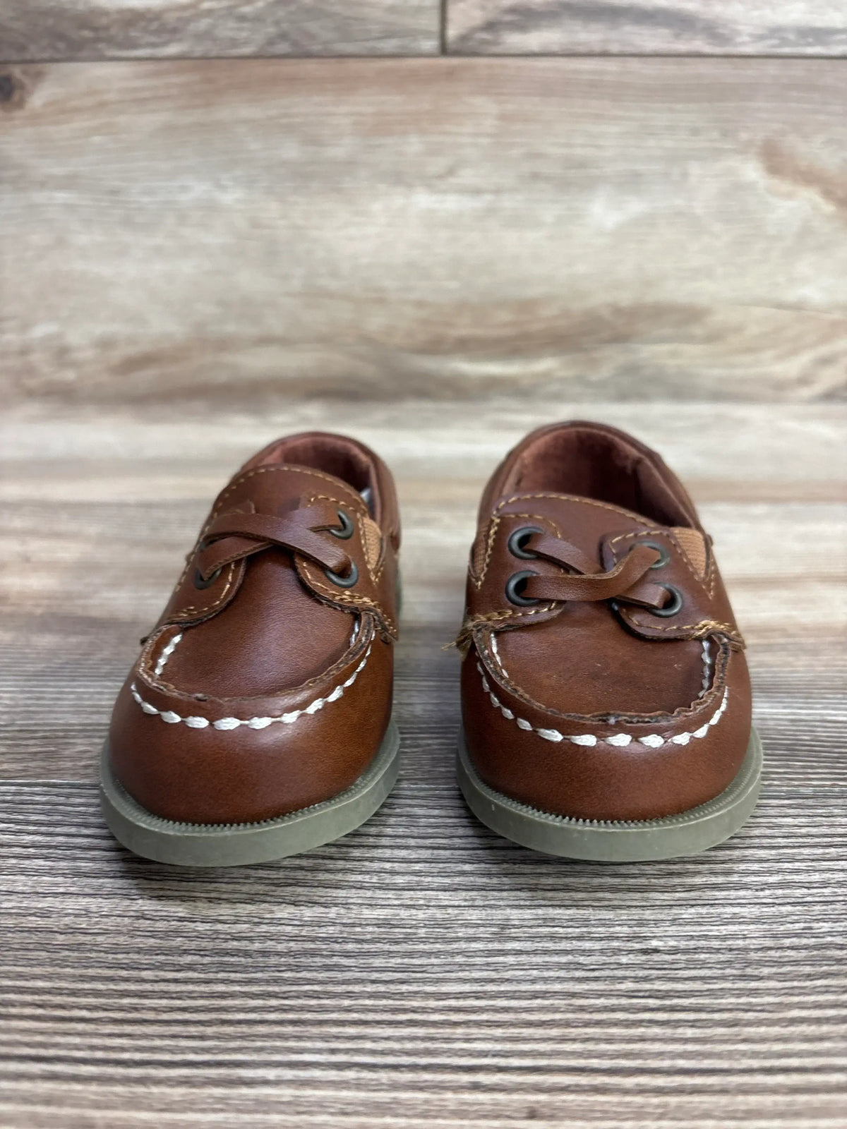 Pair of brown toddler boat shoes with white stitching on a wood surface at children's resale store