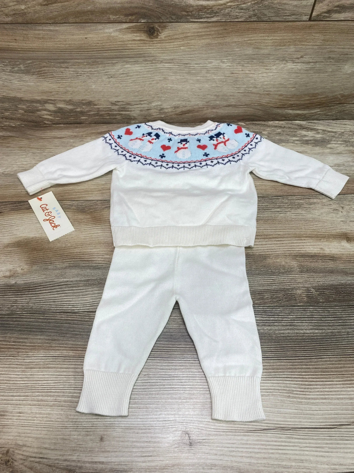 Flat lay of Cat & Jack 2-piece white baby sweater and pants showing fair isle snowman yoke and ribbed cuffs on wood background