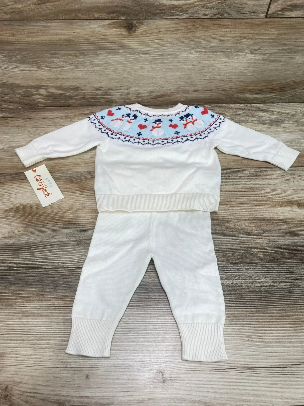 Flat lay of Cat & Jack 2-piece white baby sweater and pants showing fair isle snowman yoke and ribbed cuffs on wood background
