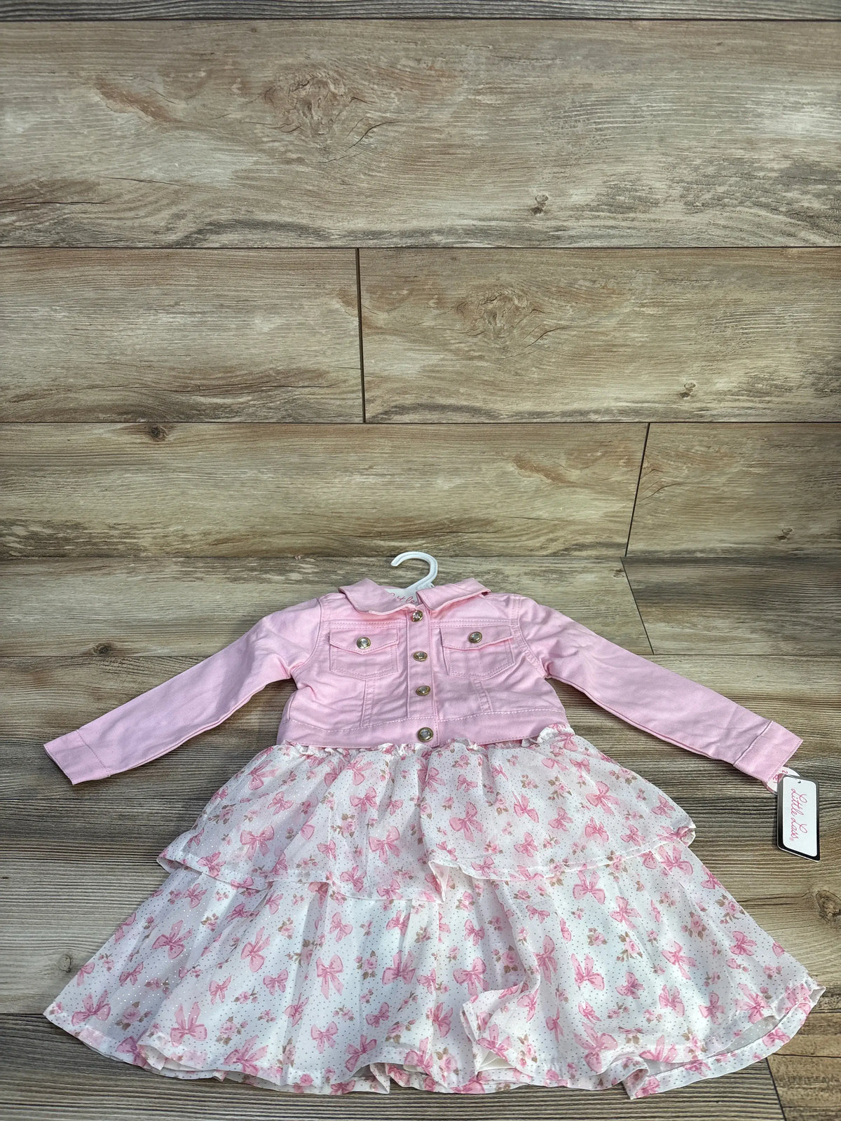 Front view of pink Little Lass toddler jacket and dress set showcasing a floral layered skirt on a wood-look floor