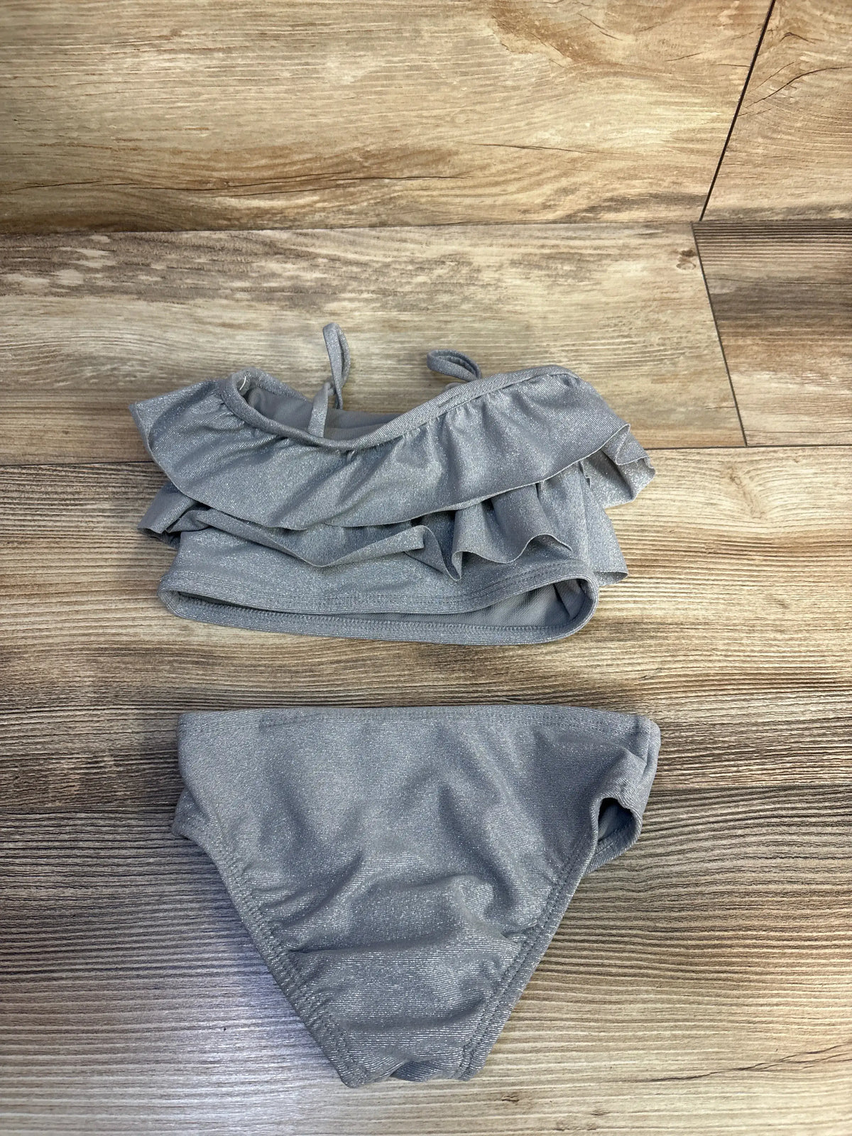 Top-down view of Baby Gap two-piece silver shiny tankini showing ruffled tank top and matching bottoms on wood background