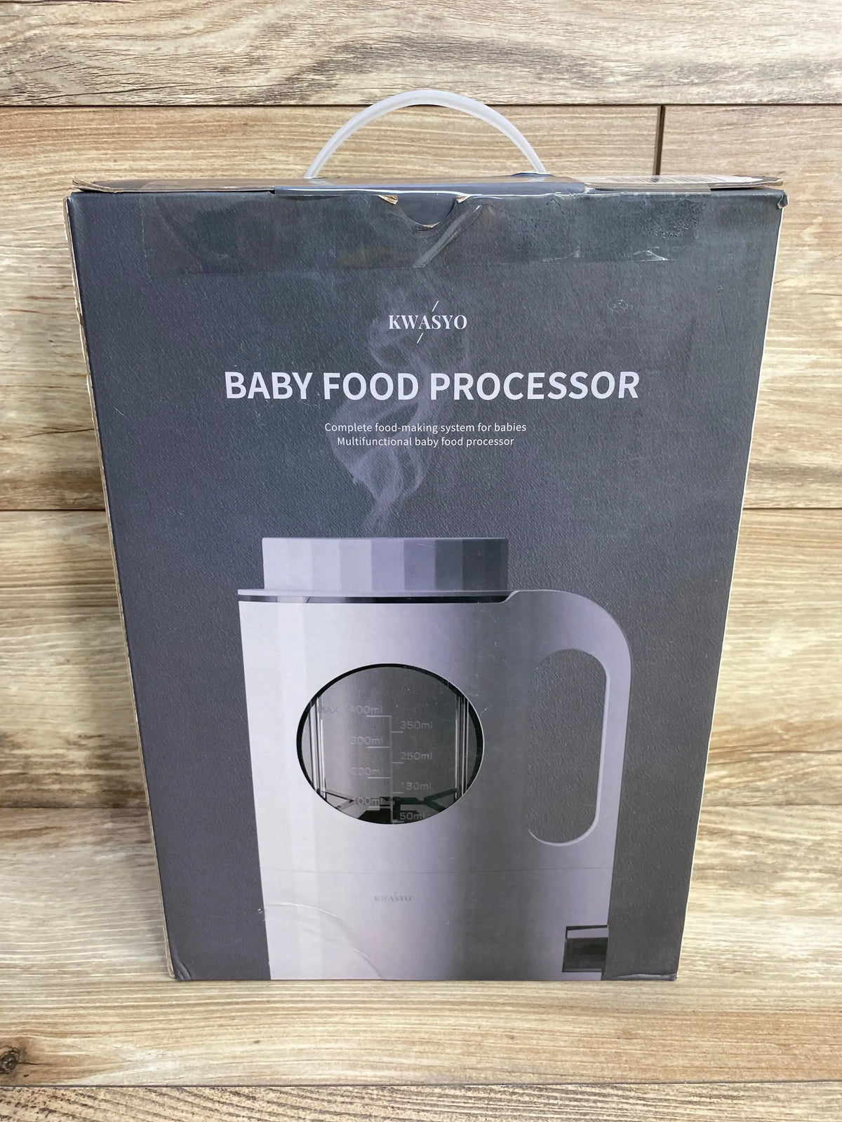 Front view of KWASYO baby food processor box showing BABY FOOD PROCESSOR headline and white unit with handle on wood
