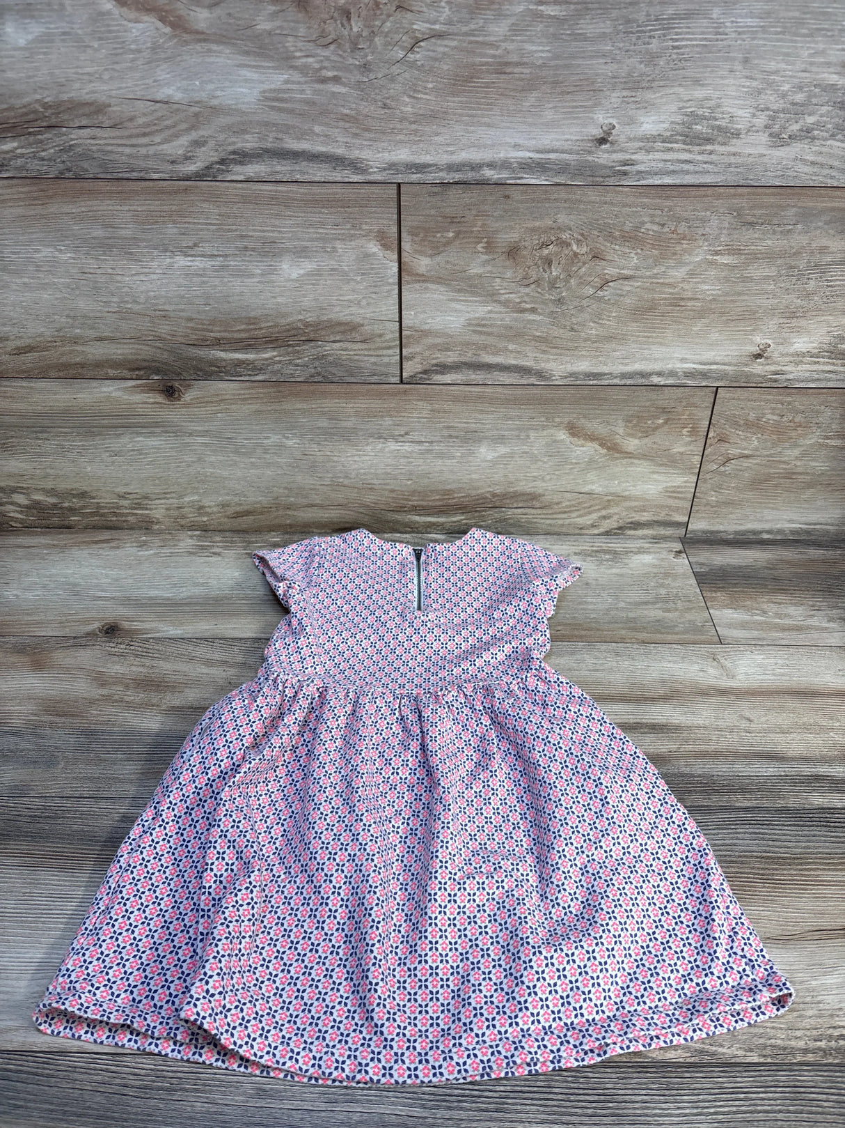 Flat lay of Carter's pink toddler dress size 4T showcasing small geometric floral pattern, cap sleeves, gathered skirt and back zipper on wood floor background