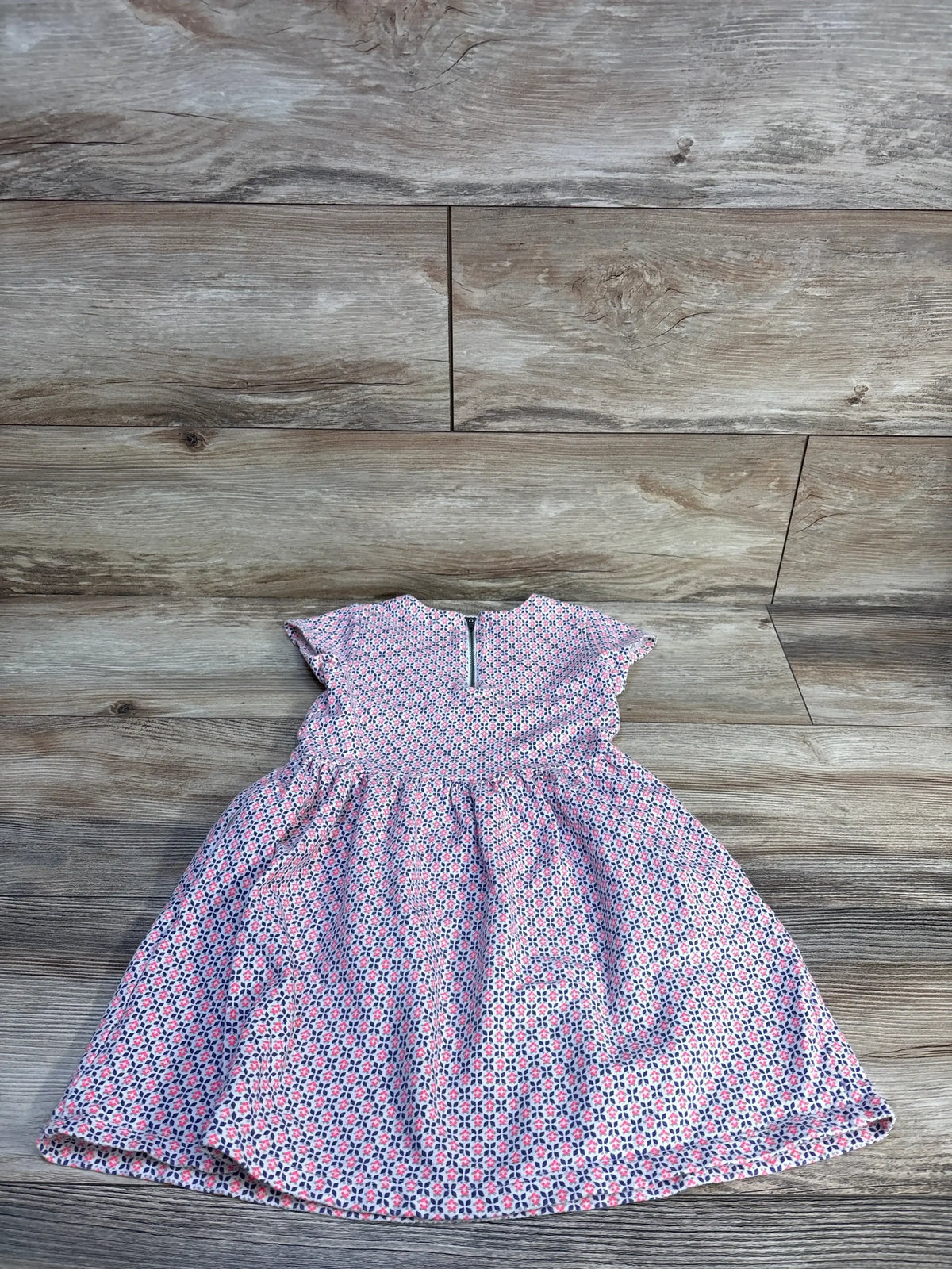 Flat lay of Carter's pink toddler dress size 4T showcasing small geometric floral pattern, cap sleeves, gathered skirt and back zipper on wood floor background