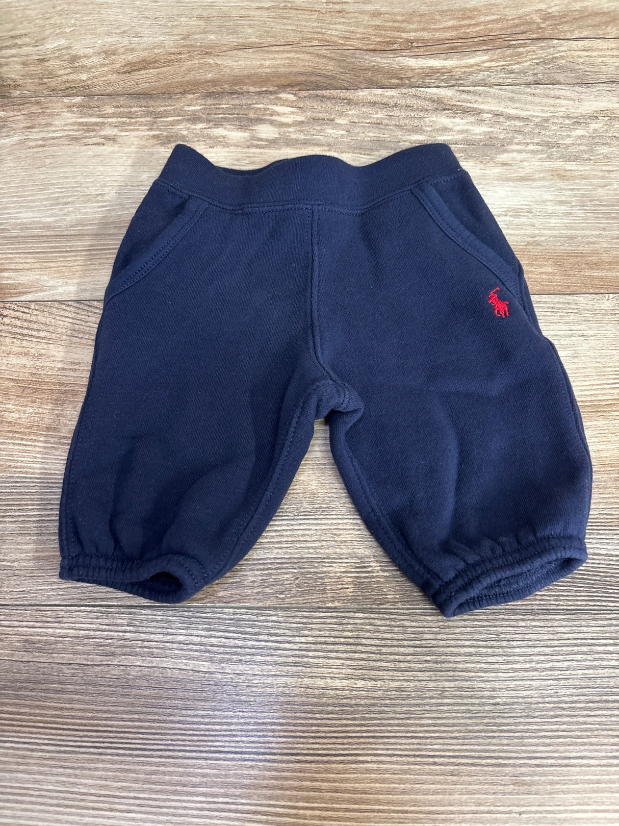 Navy blue baby jogger pants with elastic waistband and red logo on wooden background