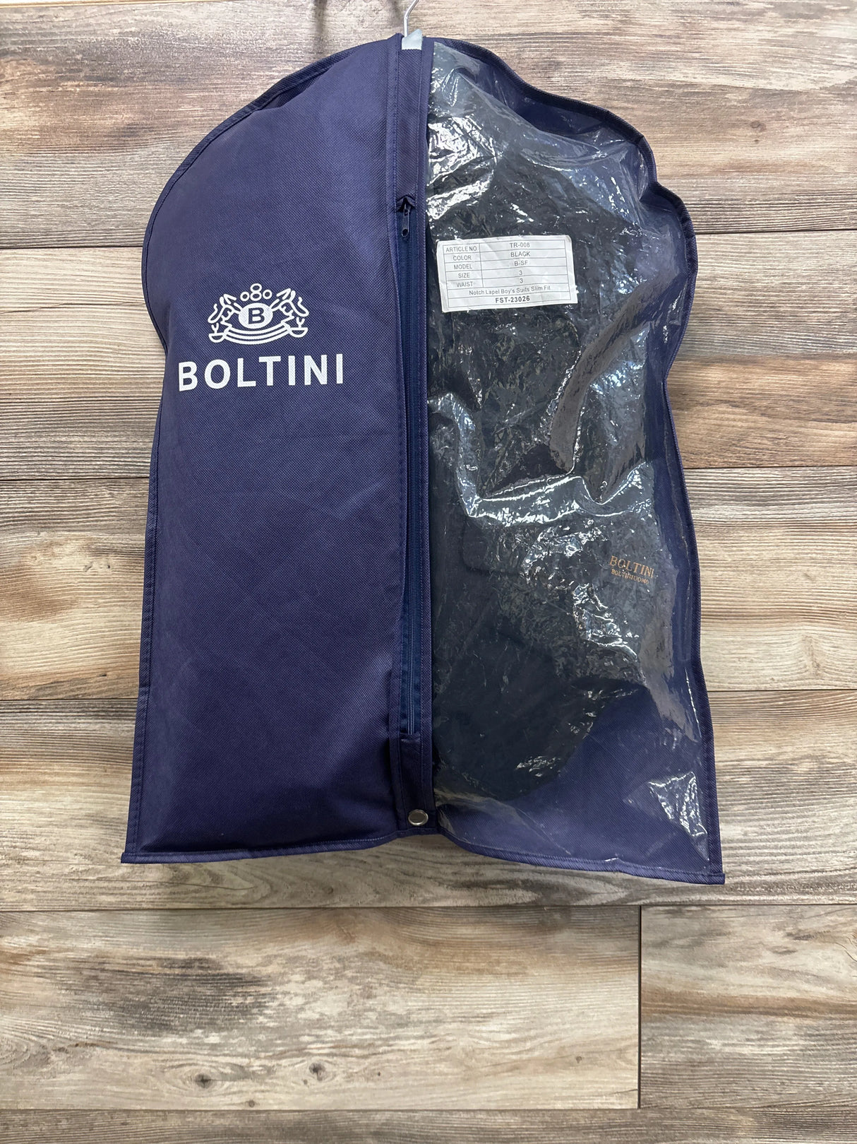 Front view of Boltini black four-piece suit set in an open garment bag on a wood floor