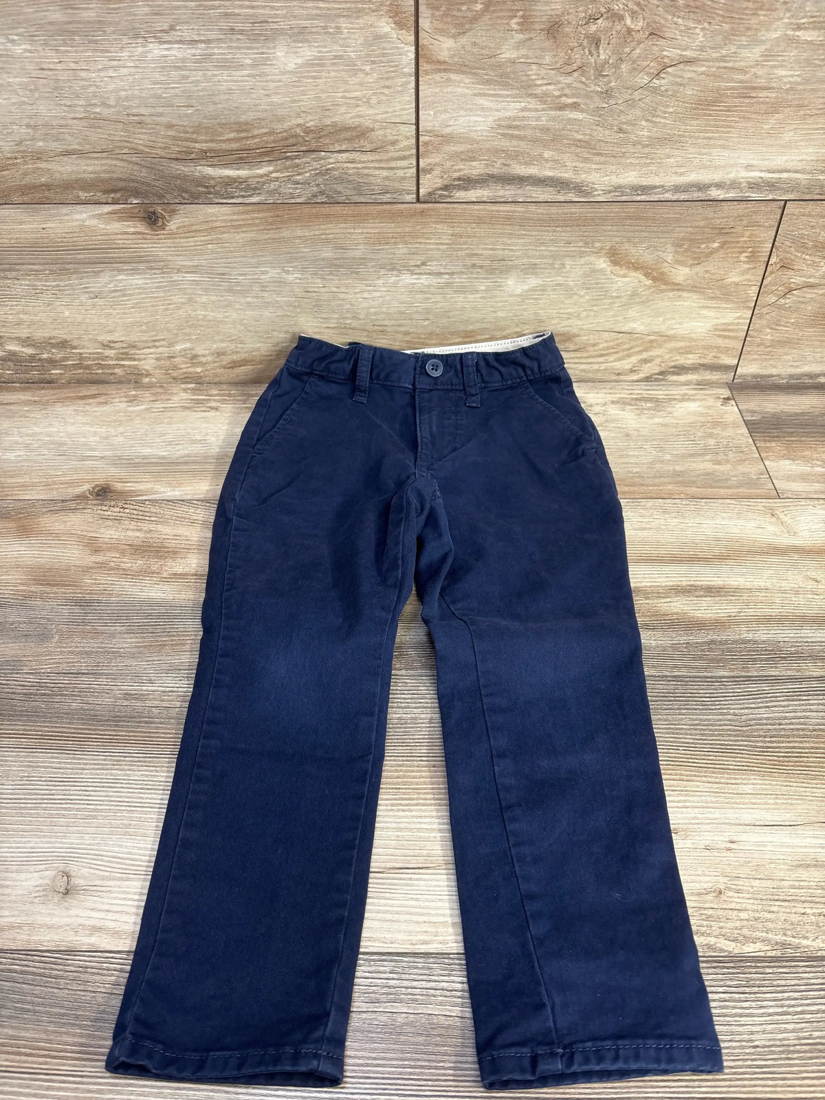 Front view of navy Gap Kids classic chino pants showcasing button closure, belt loops and front pockets on wood floor