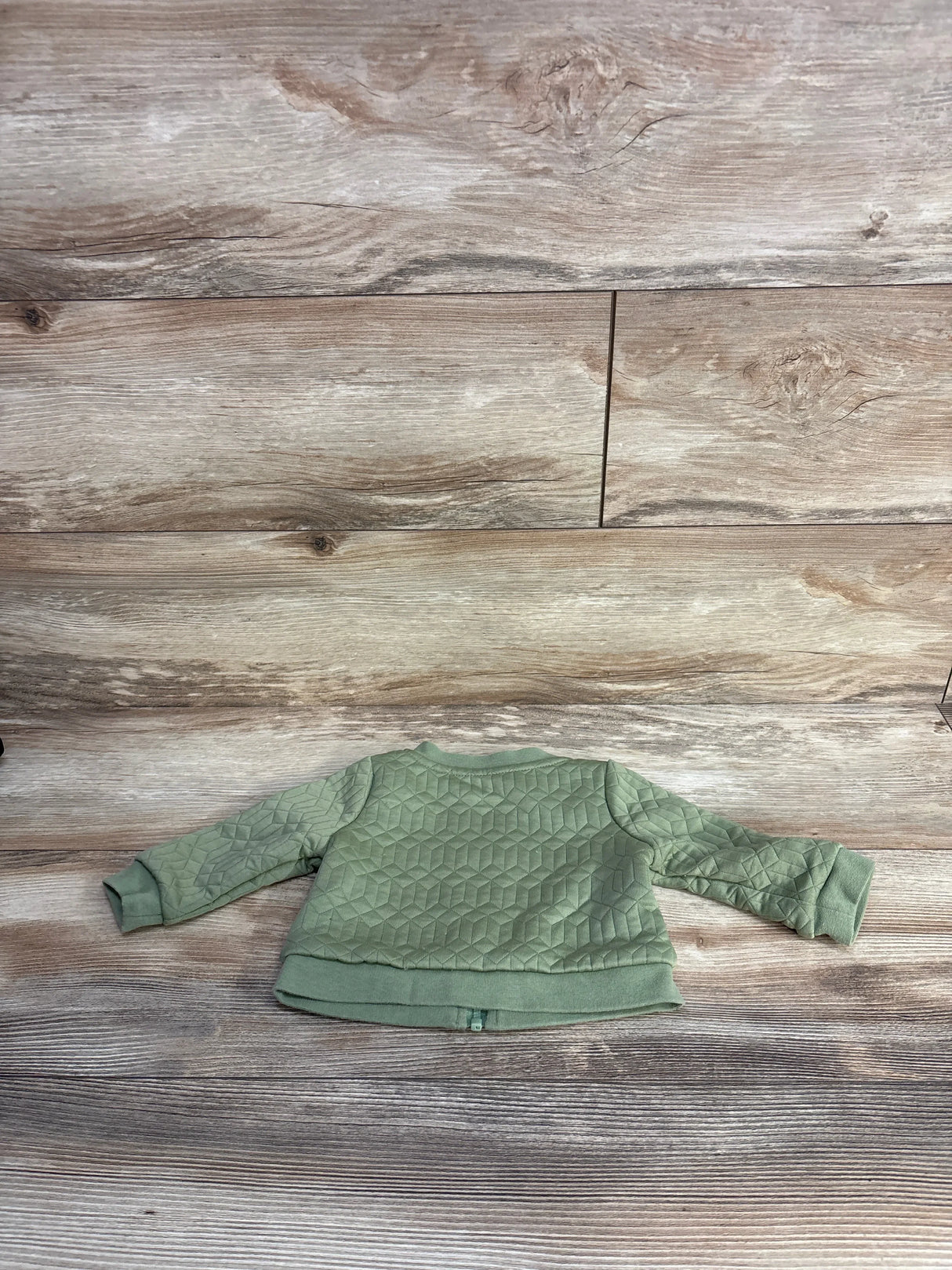 Baby green quilted long sleeve sweater laid flat on wooden floor background