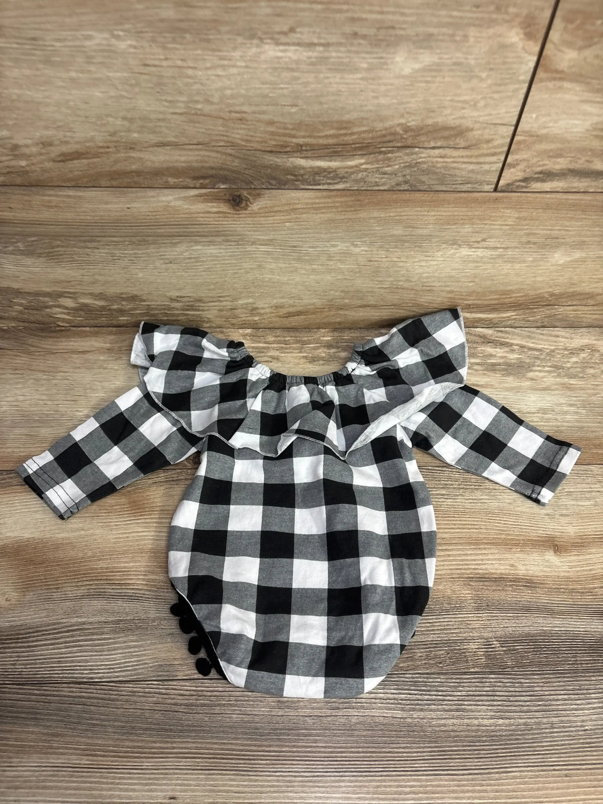 Black and white checkered baby girl long sleeve romper with ruffle detail on wooden floor