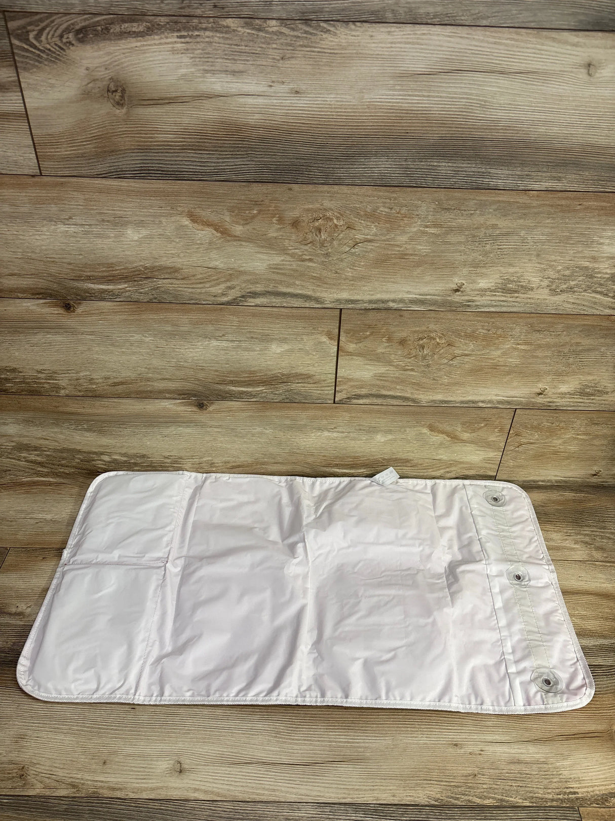 Top-down view of bath kneeling pad with organizer showing three snap buttons and pockets on wooden floor
