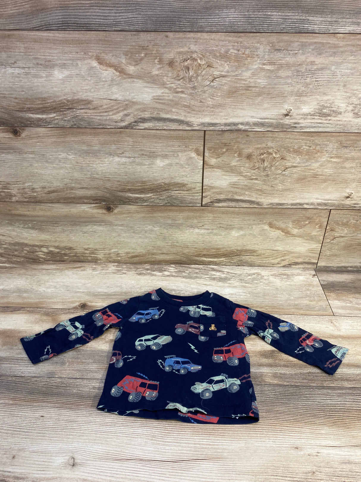 Front view of Baby Gap navy long-sleeve pocket shirt (18-24M) showcasing all-over toy truck print, laid flat on wood background