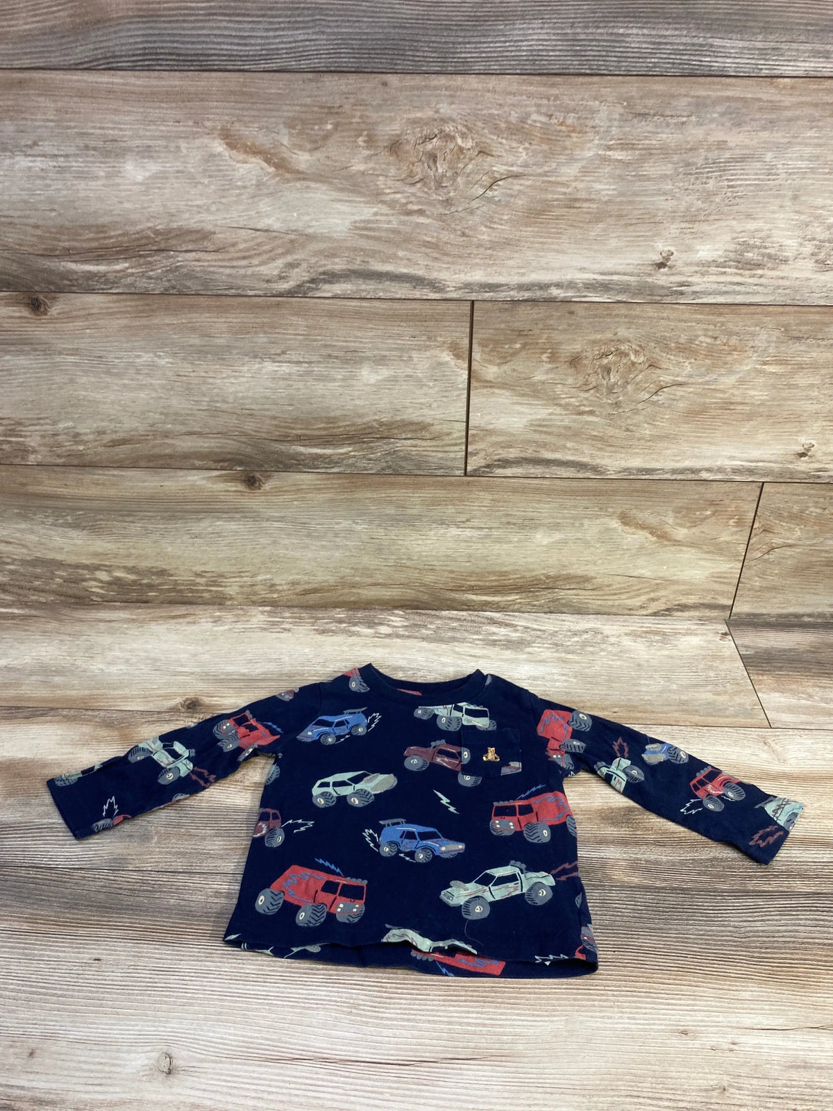 Front view of Baby Gap navy long-sleeve pocket shirt (18-24M) showcasing all-over toy truck print, laid flat on wood background