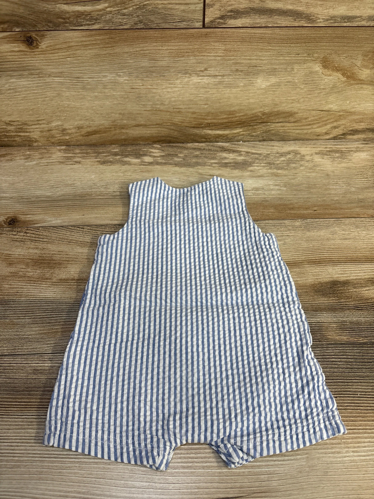 Back view of striped shortie romper showcasing blue and white seersucker vertical stripes on wood background