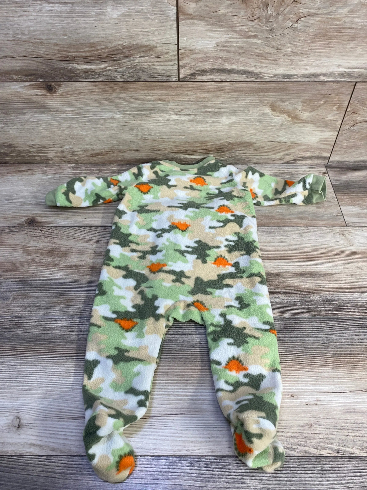 Flat lay of Mon Cheri camo blanket sleeper showing fleece with green, tan and orange pattern and footed legs on wood background