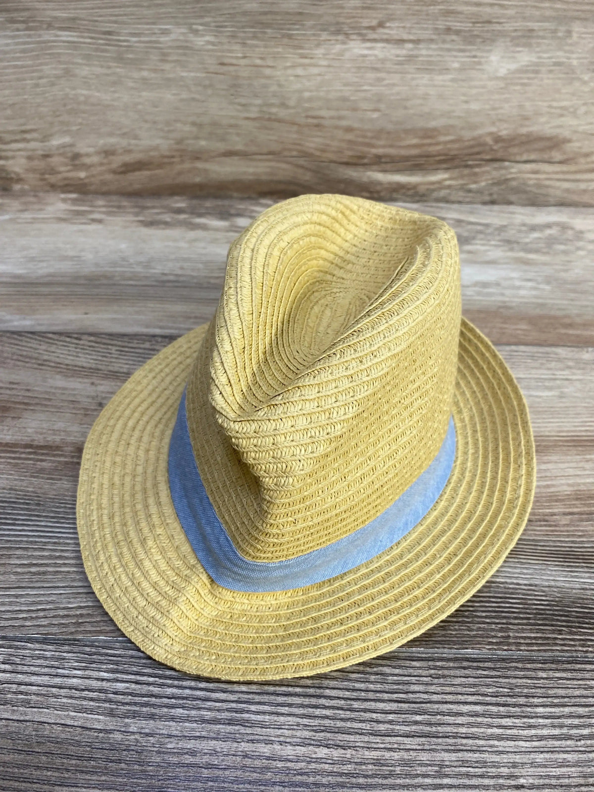 Yellow straw fedora hat with a light blue fabric band placed on wooden surface