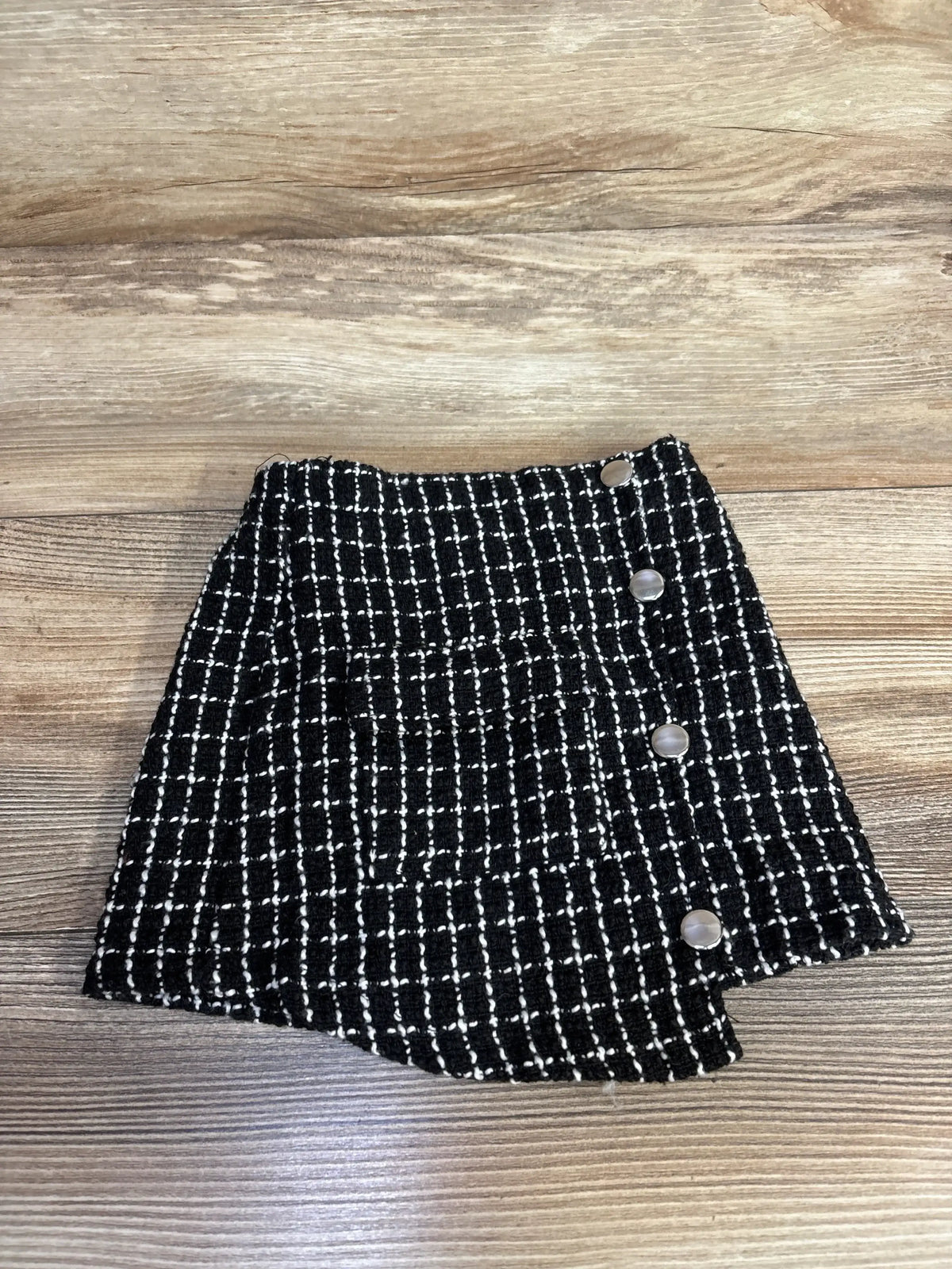 Black and white plaid tweed mini skirt with buttons, displayed on wooden background