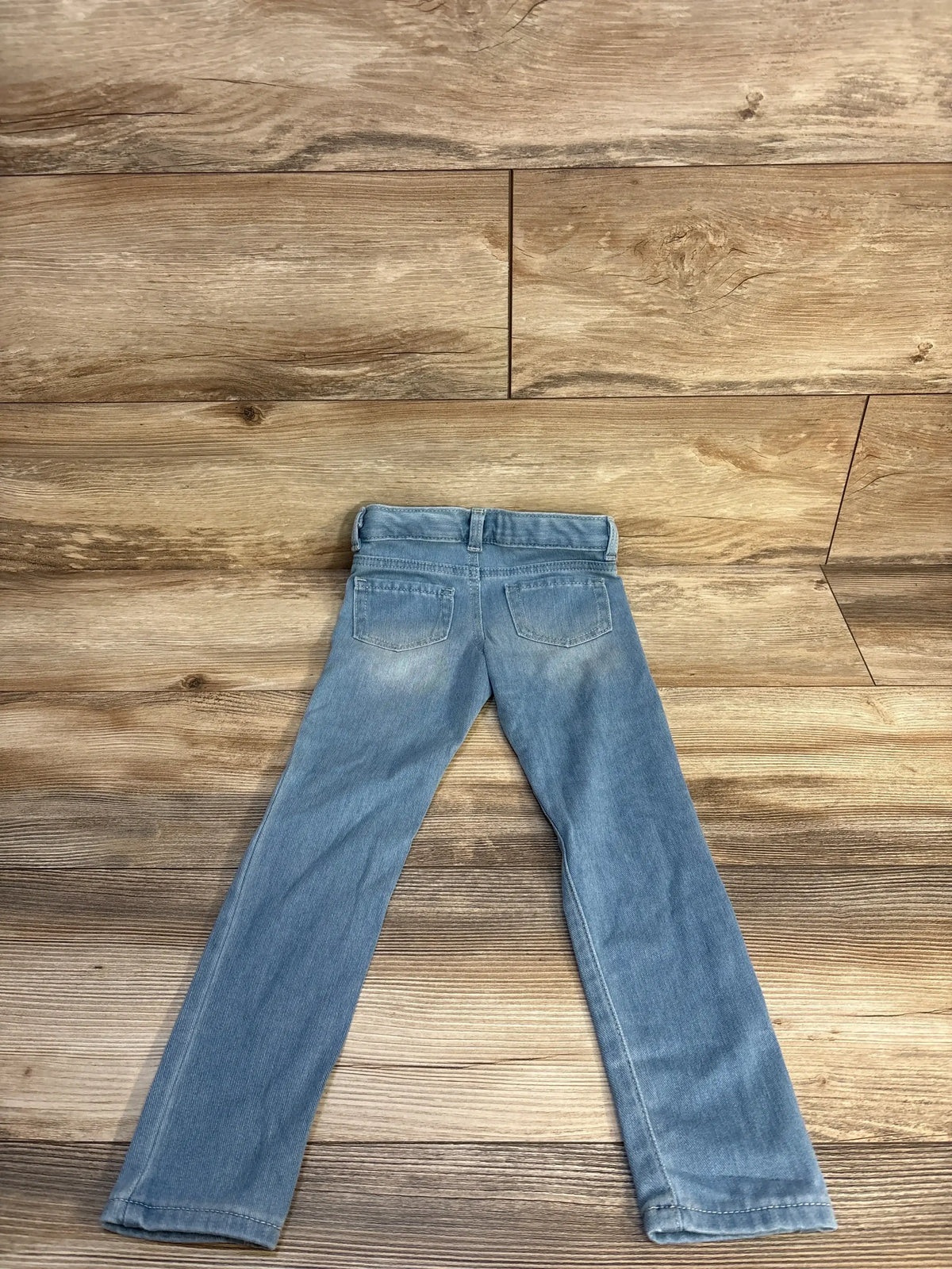 Light blue children's jeans laid flat on a wood background, back pockets visible