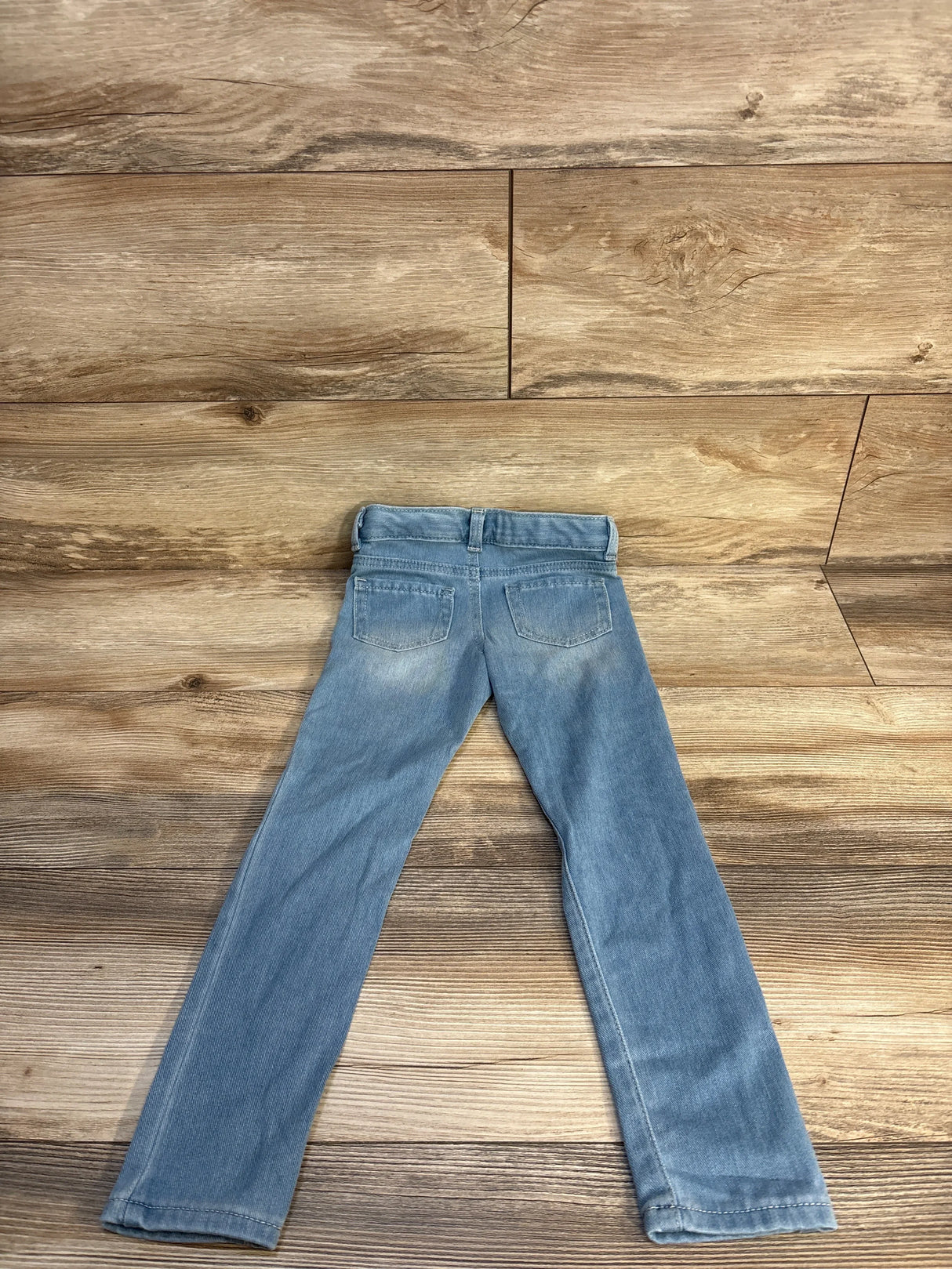 Light blue children's jeans laid flat on a wood background, back pockets visible