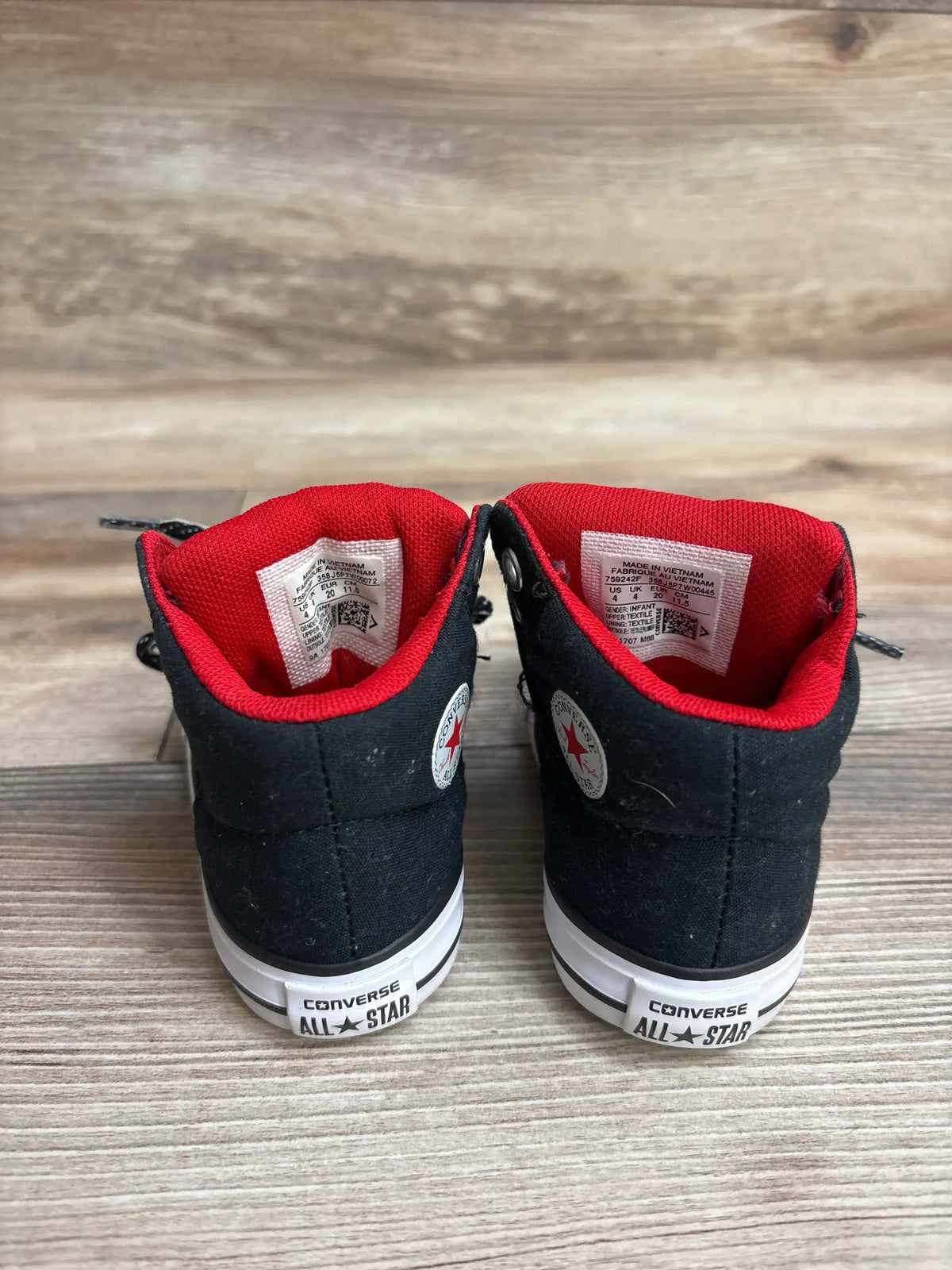 Rear view of black Converse All Star infant sneakers with red inner lining on wooden floor