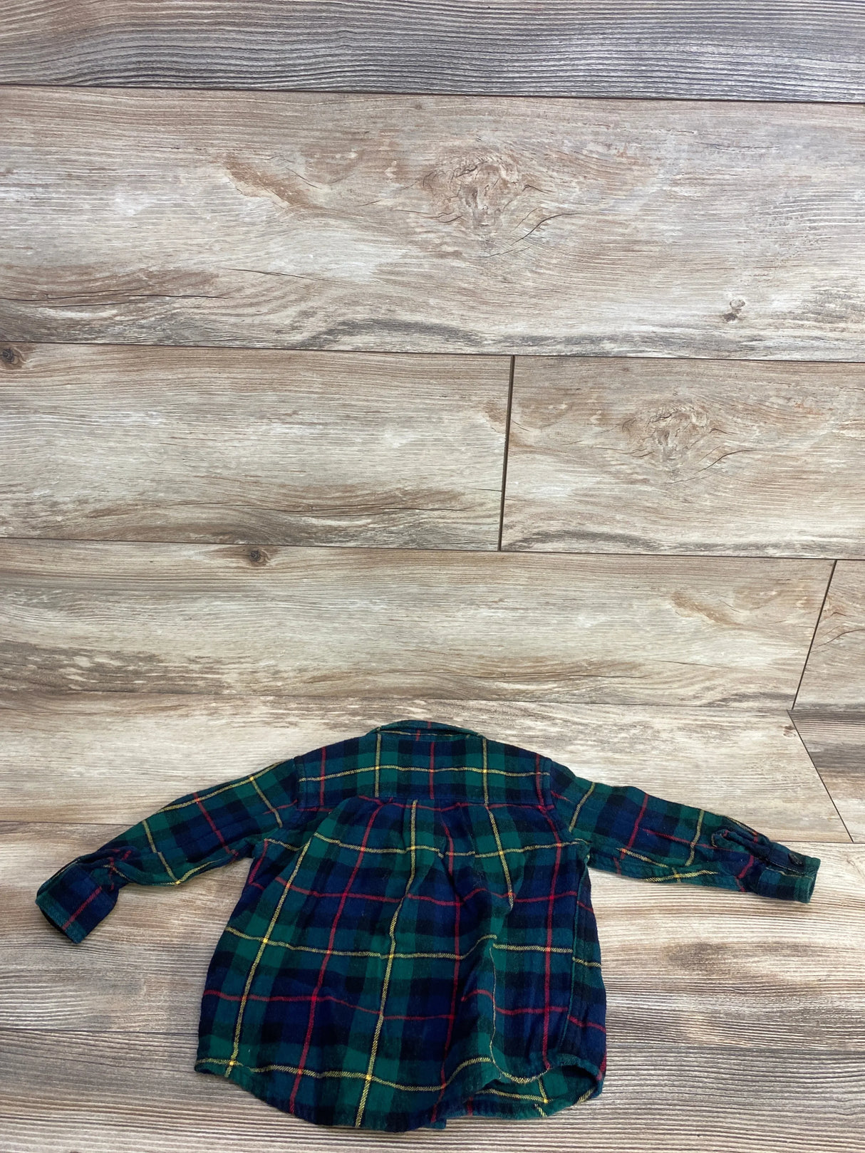 Children's green, navy, red, and yellow plaid long sleeve shirt on wood floor background