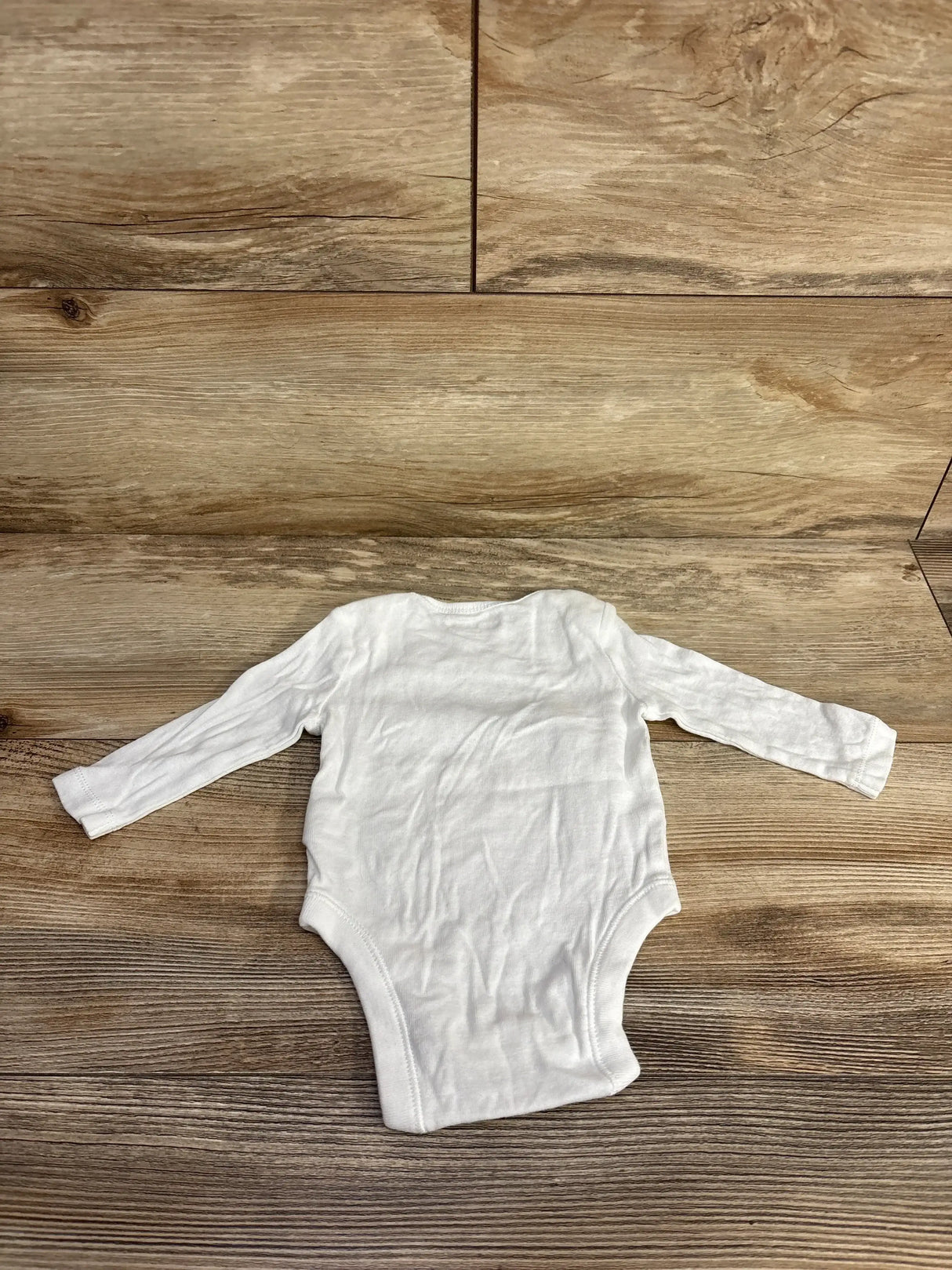 White long-sleeve baby onesie on wood floor, newborn clothing for infants and toddlers