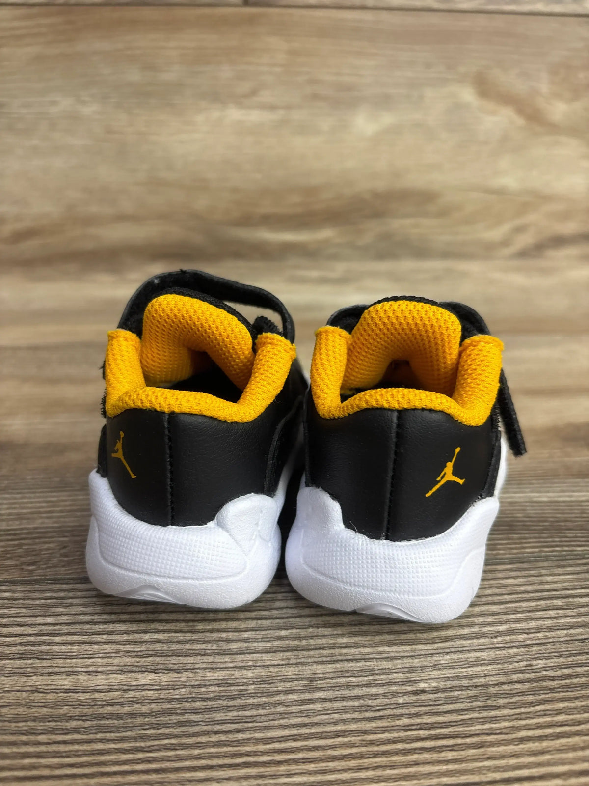 Black and yellow toddler sneakers with white soles on wood background