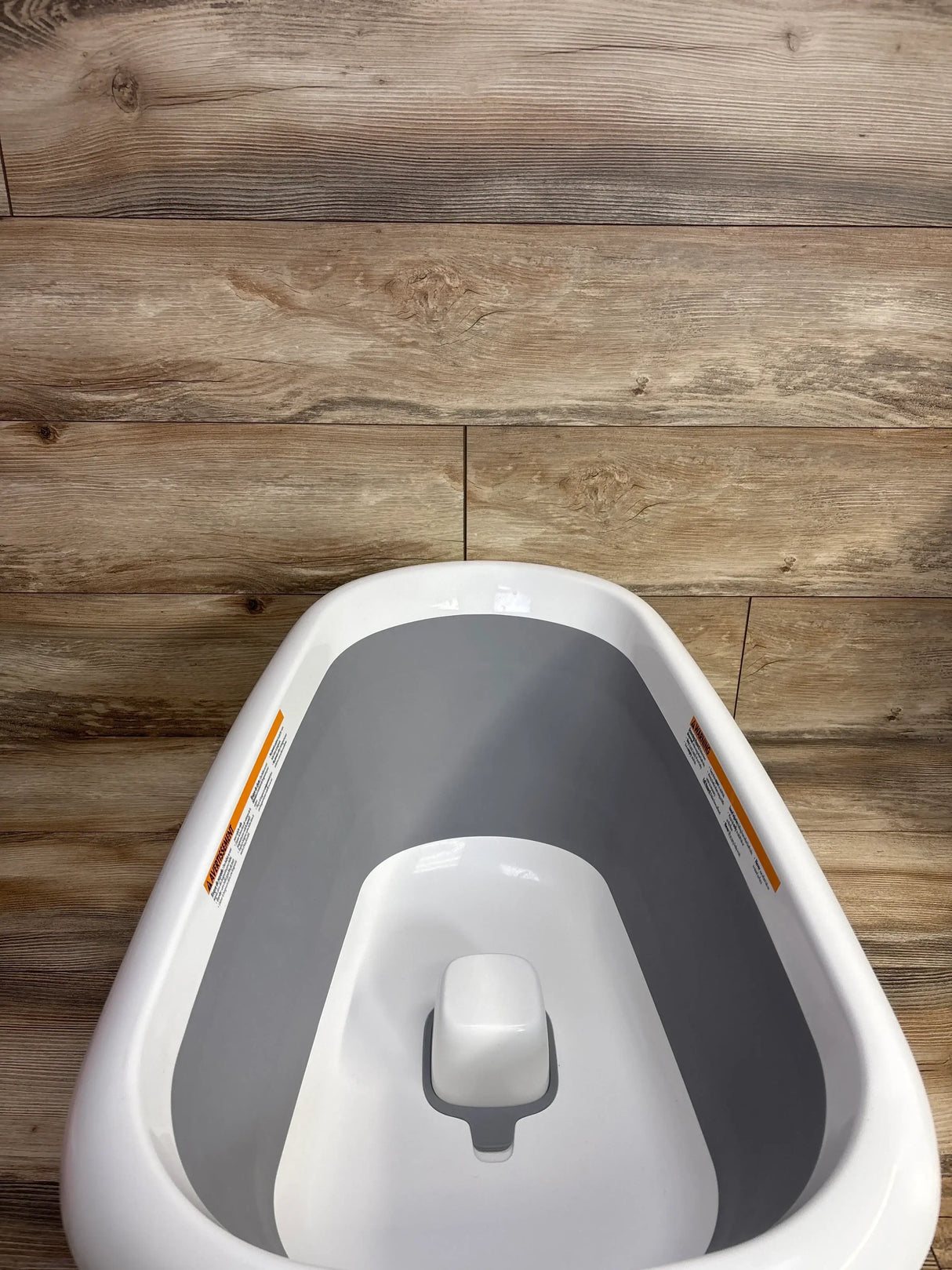 Front view of OXO Tot Splash & Store bathtub, grey and white, with foldable legs and contoured infant seat on wood floor