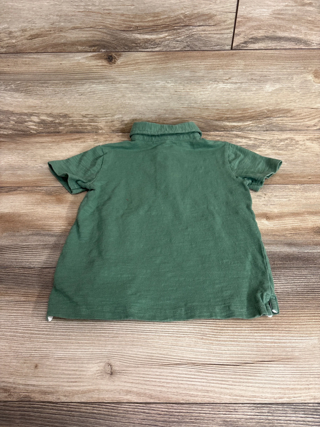 Back view of Janie and Jack green pique polo shirt (5T) showing short sleeves, folded collar and side vents on wood background