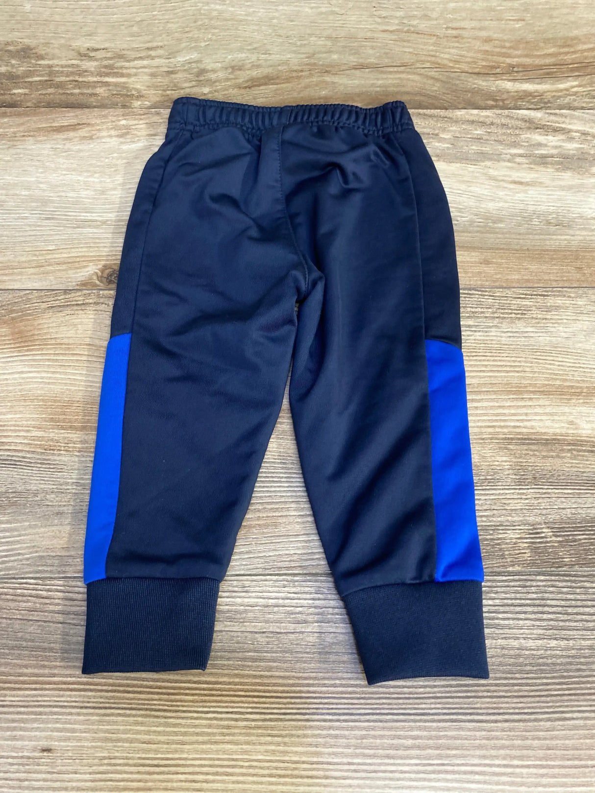 Flat lay of navy Nike joggers showing elastic waistband, ribbed ankle cuffs and blue side panels on wood background