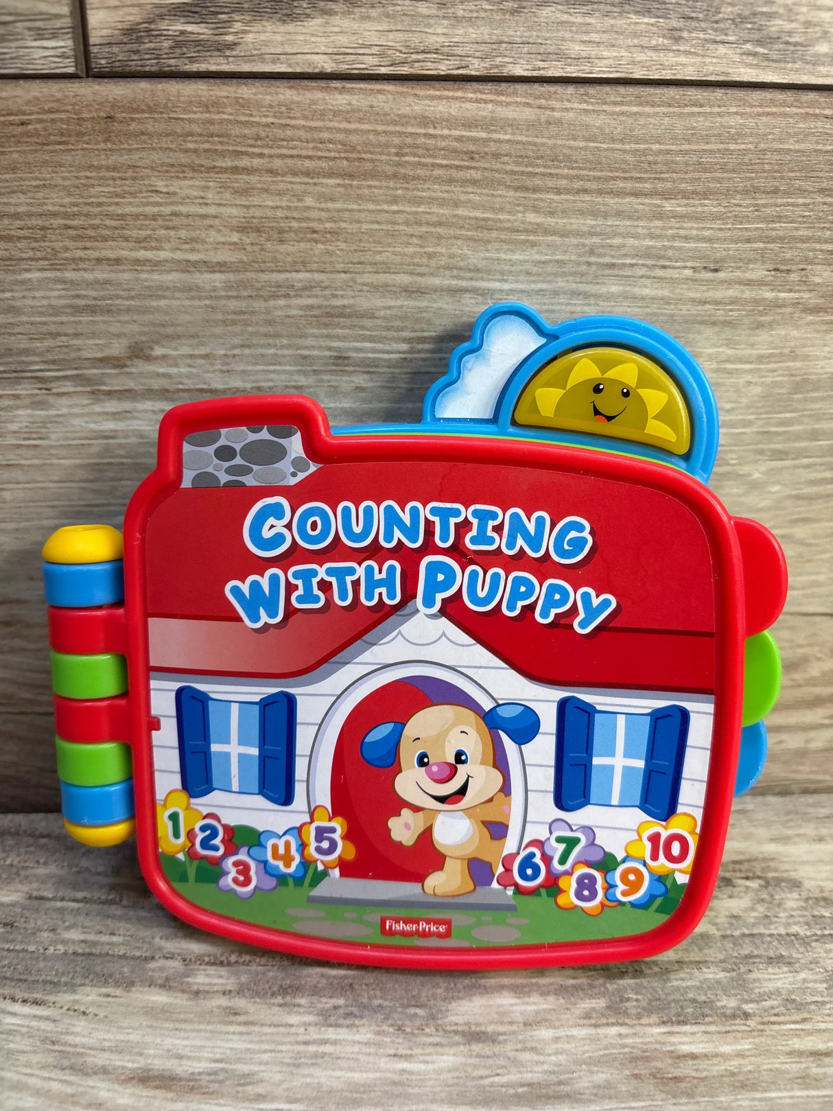 Front view of Fisher-Price Counting with Puppy electronic book showcasing colorful cover with smiling puppy, numbers 1 to 10, and side plastic tabs on wood-grain surface