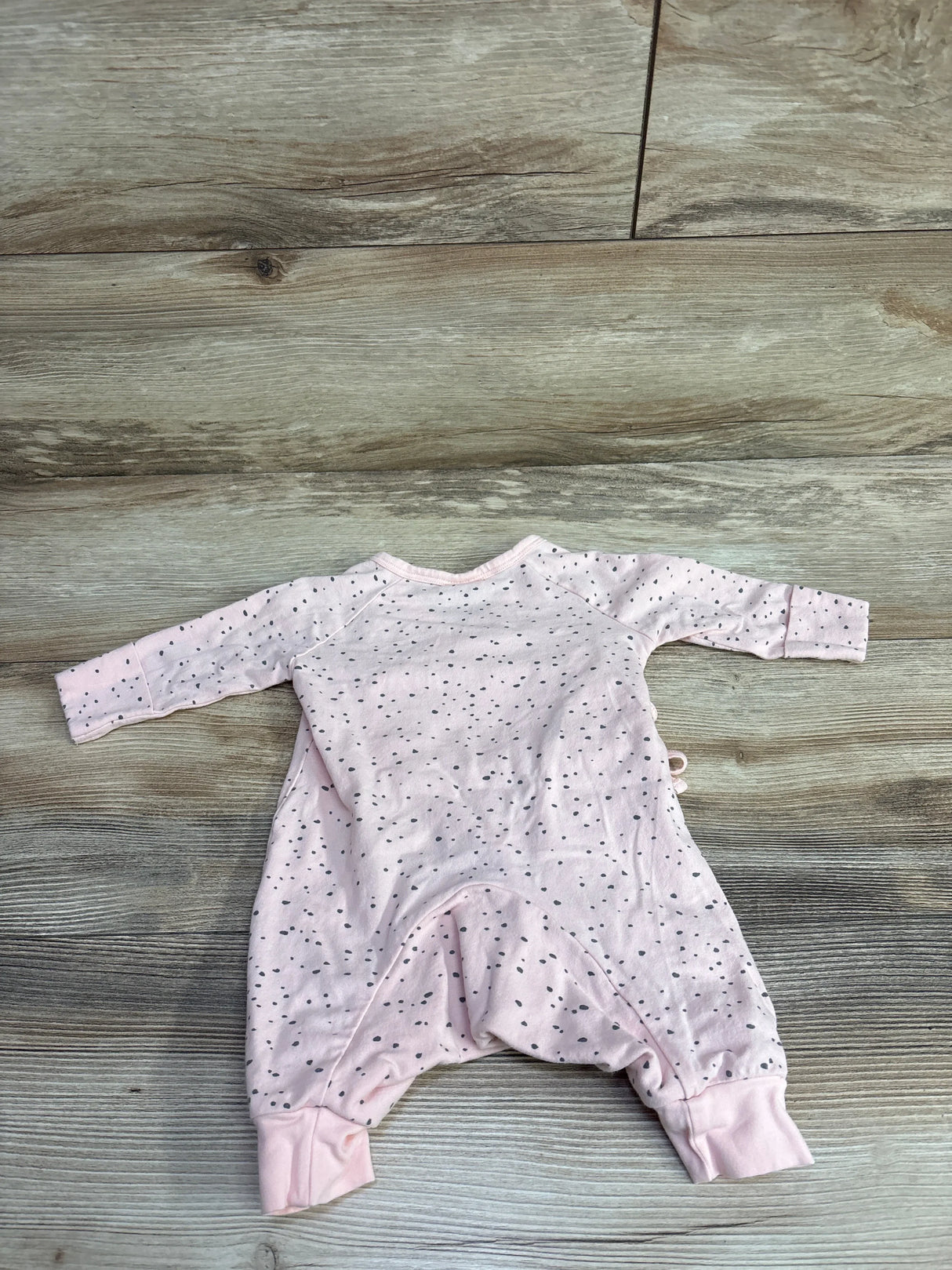 Light pink dotted long-sleeve baby romper laid flat on wood floor, kids clothes resale