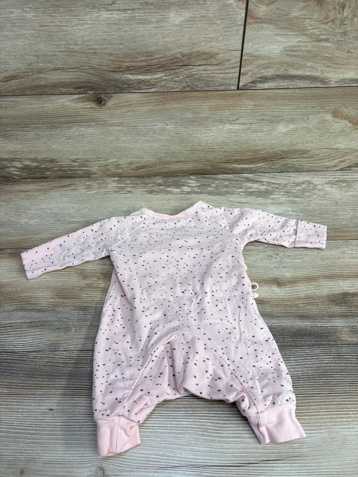 Light pink dotted long-sleeve baby romper laid flat on wood floor, kids clothes resale