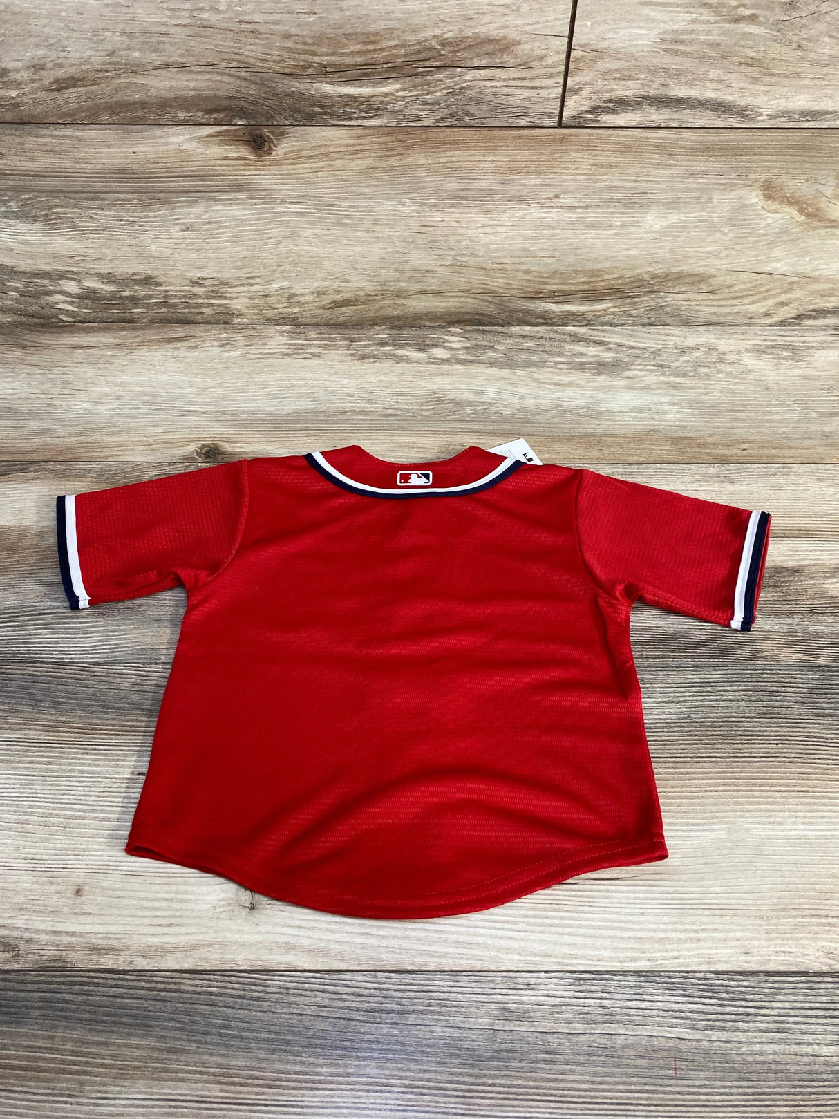 Back view of Washington Nationals toddler red replica jersey showing MLB logo at neckline and navy-white sleeve trim on wood floor background