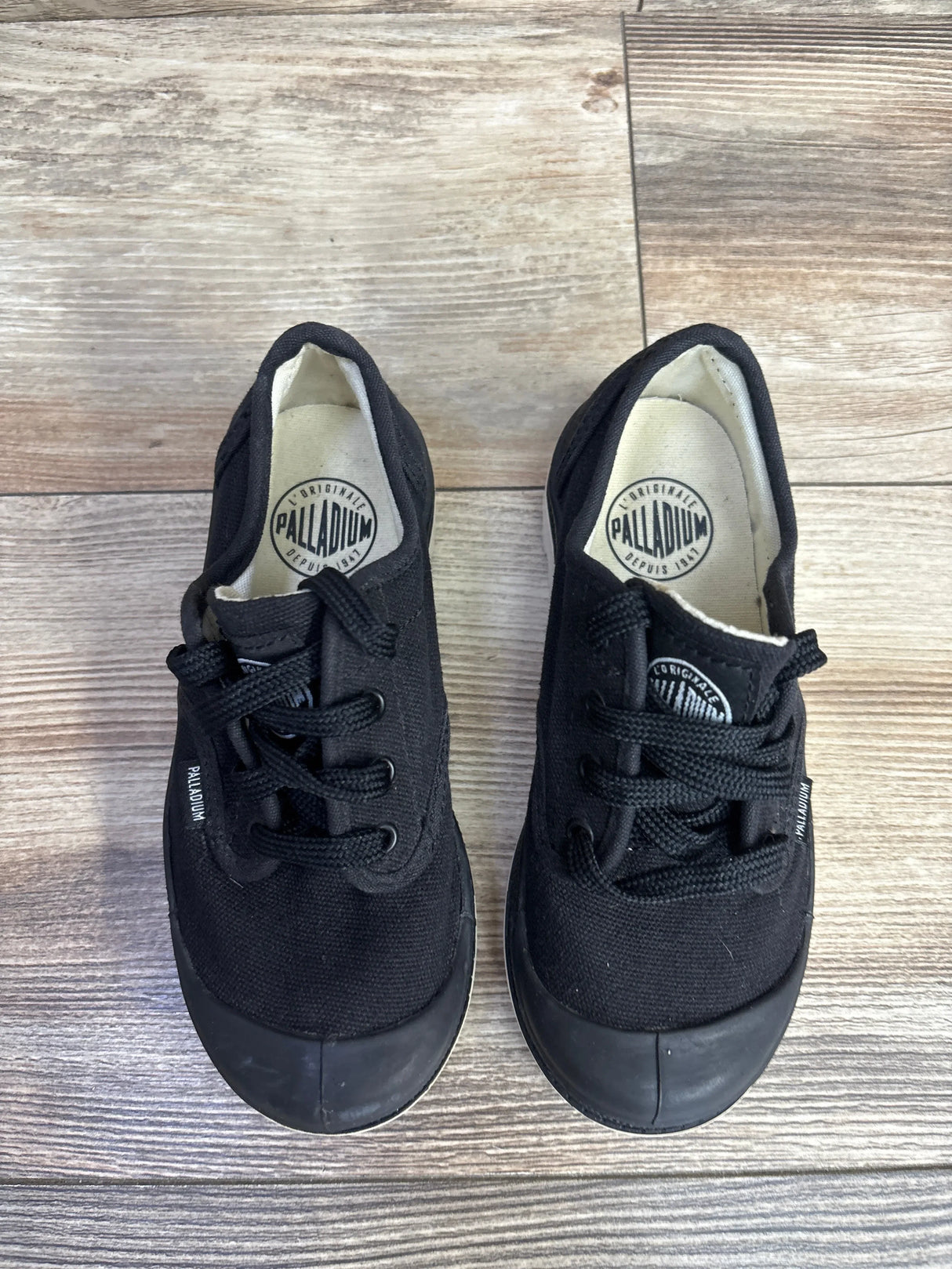 Pair of black Palladium canvas kids sneakers with rubber toe caps on wood floor