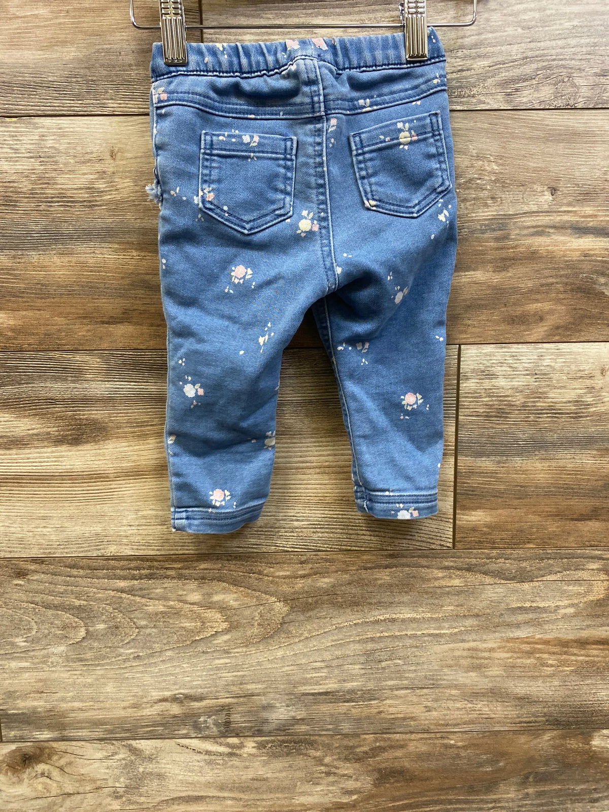 Rear view of Cat and Jack pull on jeggings showcasing blue floral print, back pockets, and elastic waist on a wood background